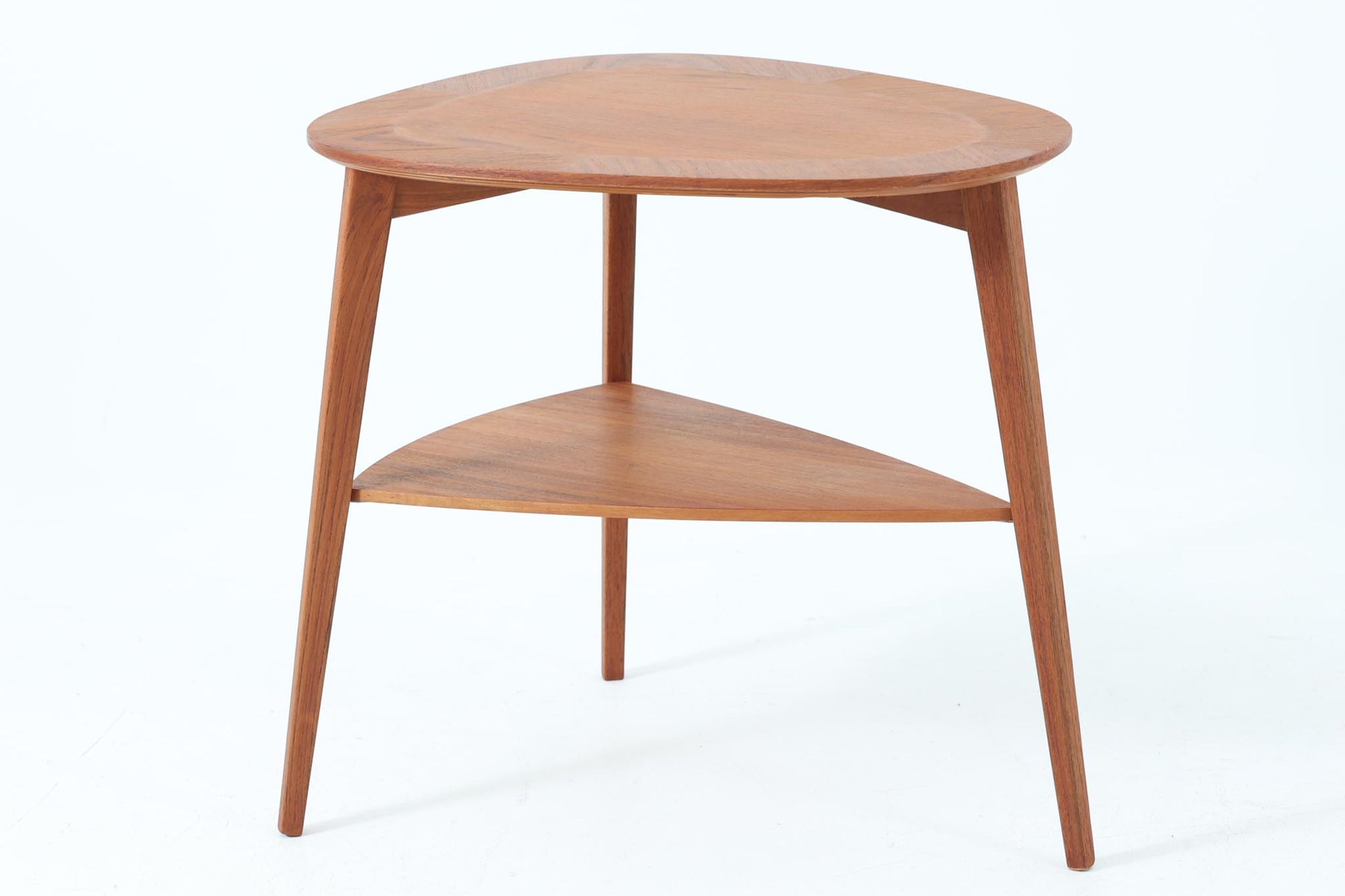 Holger Georg Jensen（ホルガー・ジョージ・イェンセン）によってデザインされ、Kubus moblerから製造されたデンマーク製ビンテージのサイドテーブルです。有機的な曲線を描く天板と、それを支える3本脚の構造が美しいバランスを保っています。天板下には同形状の棚板が設けられており、雑誌や小物の収納にも便利です。素材には艶やかなチーク材が用いられ、天板の木目の美しさも際立っています。北欧モダンを感じさせる上品な佇まいで、ソファサイドやベッドサイドにおすすめの一台です。