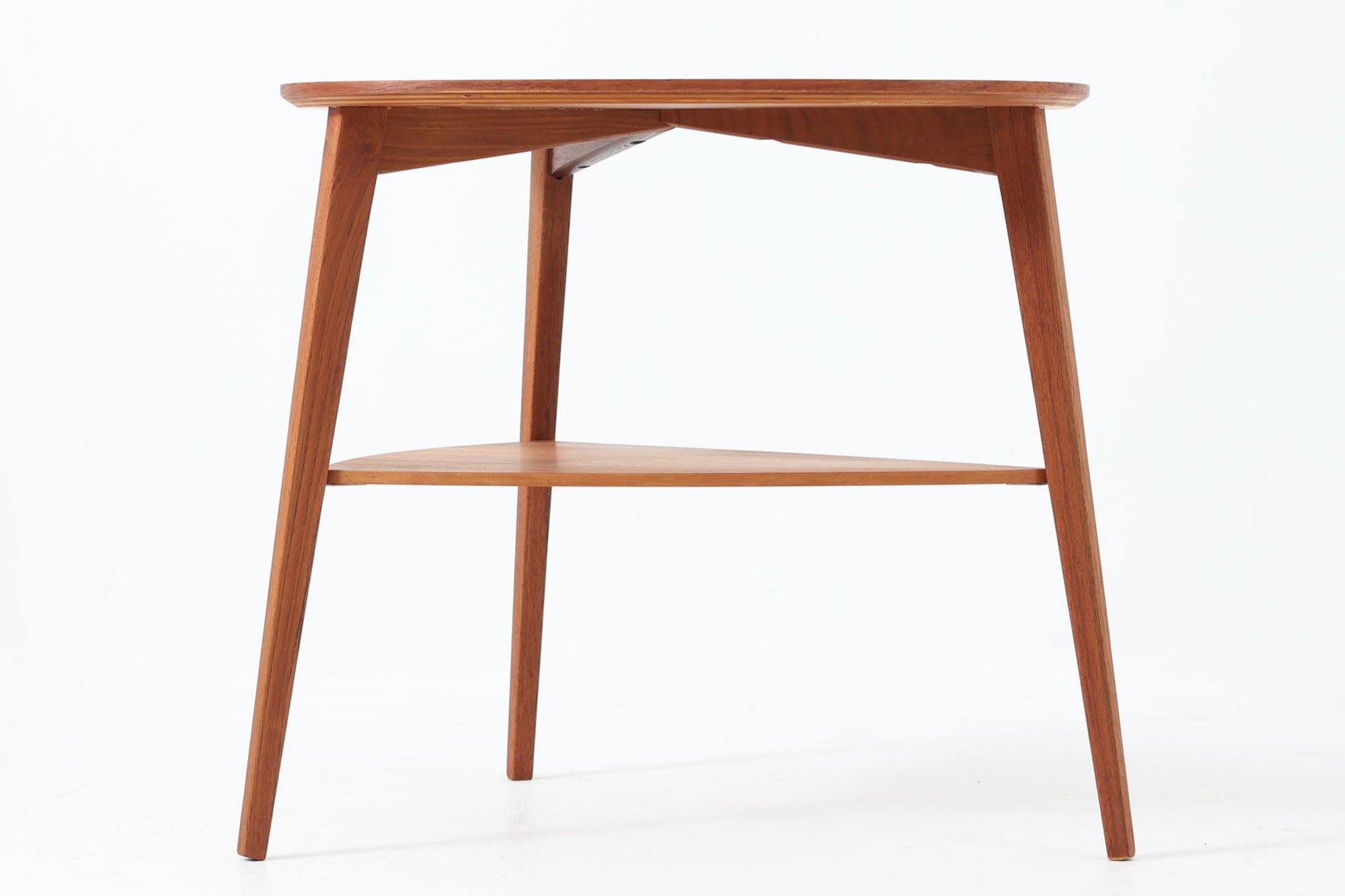 Holger Georg Jensen（ホルガー・ジョージ・イェンセン）によってデザインされ、Kubus moblerから製造されたデンマーク製ビンテージのサイドテーブルです。有機的な曲線を描く天板と、それを支える3本脚の構造が美しいバランスを保っています。天板下には同形状の棚板が設けられており、雑誌や小物の収納にも便利です。素材には艶やかなチーク材が用いられ、天板の木目の美しさも際立っています。北欧モダンを感じさせる上品な佇まいで、ソファサイドやベッドサイドにおすすめの一台です。