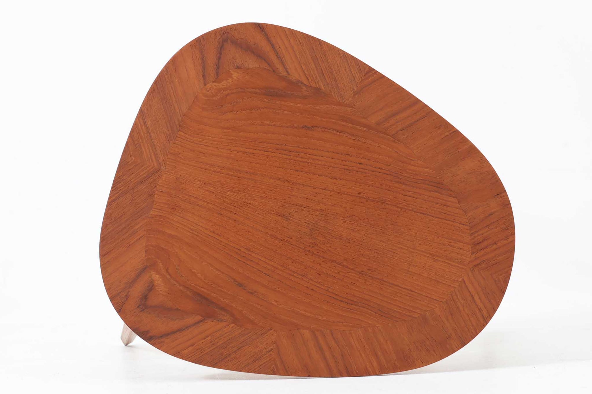 Holger Georg Jensen（ホルガー・ジョージ・イェンセン）によってデザインされ、Kubus moblerから製造されたデンマーク製ビンテージのサイドテーブルです。有機的な曲線を描く天板と、それを支える3本脚の構造が美しいバランスを保っています。天板下には同形状の棚板が設けられており、雑誌や小物の収納にも便利です。素材には艶やかなチーク材が用いられ、天板の木目の美しさも際立っています。北欧モダンを感じさせる上品な佇まいで、ソファサイドやベッドサイドにおすすめの一台です。