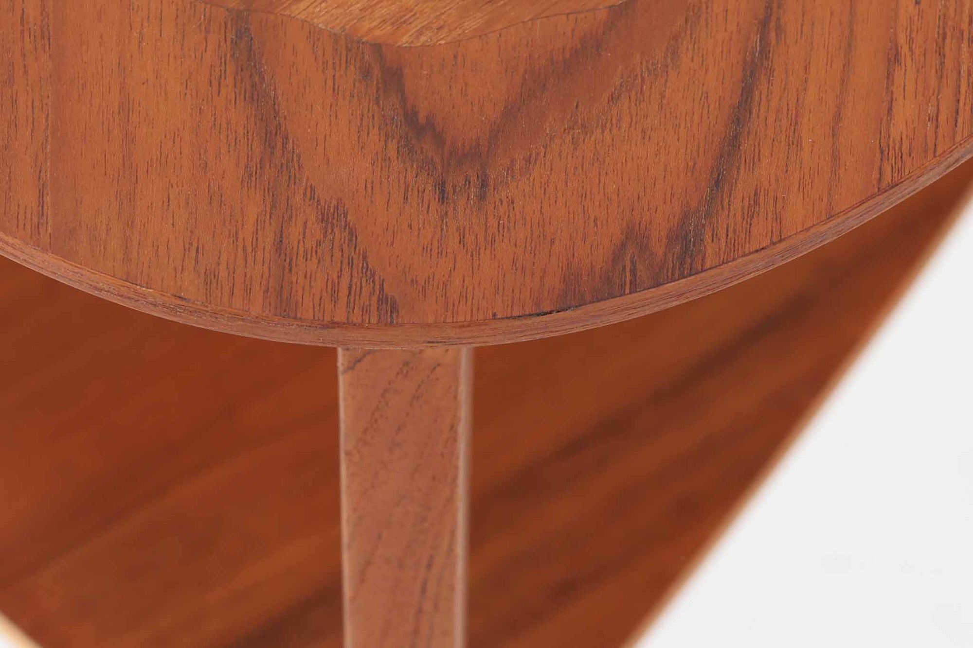 Holger Georg Jensen（ホルガー・ジョージ・イェンセン）によってデザインされ、Kubus moblerから製造されたデンマーク製ビンテージのサイドテーブルです。有機的な曲線を描く天板と、それを支える3本脚の構造が美しいバランスを保っています。天板下には同形状の棚板が設けられており、雑誌や小物の収納にも便利です。素材には艶やかなチーク材が用いられ、天板の木目の美しさも際立っています。北欧モダンを感じさせる上品な佇まいで、ソファサイドやベッドサイドにおすすめの一台です。