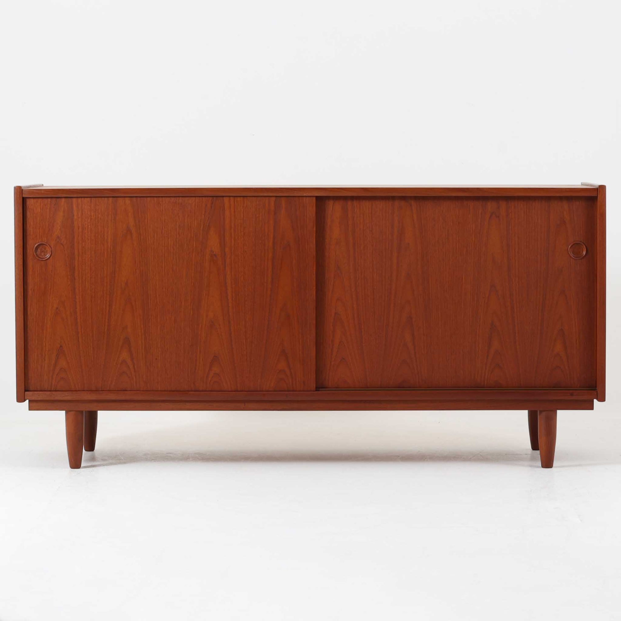 上質なチーク材を贅沢に用いたデンマーク製のボードは、幅144cmの程よいサイズ感と、丸型の掘り込み取手が印象的な引き戸デザインが特徴です。内部にはカトラリーなどの小物収納に便利な浅型引き出しと、可動棚を備えた収納スペースが左右に配置され、実用性と美しさを兼ね備えています。木目の表情豊かで、北欧ビンテージ家具らしい温かみと洗練された雰囲気を持ち、リビングやダイニングでの収納家具として活躍します。