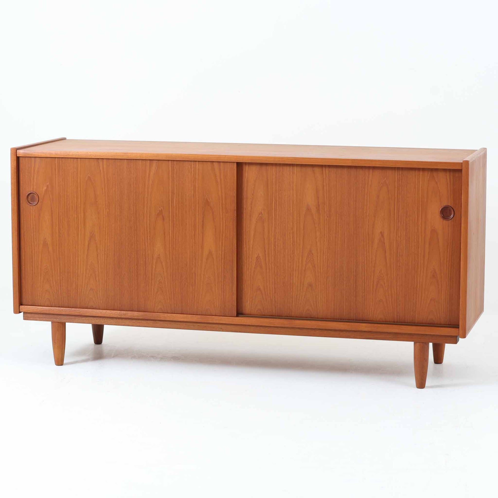 チーク材の美しい木目と滑らかな質感が際立つこちらのローボードは、収納力とデザイン性を兼ね備えた北欧ビンテージ家具です。丸い指掛けが施された引き戸を開けると、内部には仕切り棚やトレイ付きの収納スペースがあり、食器類や小物の整理に最適です。脚部は丸脚で軽やかな印象を与え、リビングのテレビ台やキャビネットとしても活躍する一台です。年月を経て深まった風合いが、空間に温かみと落ち着きをもたらします。