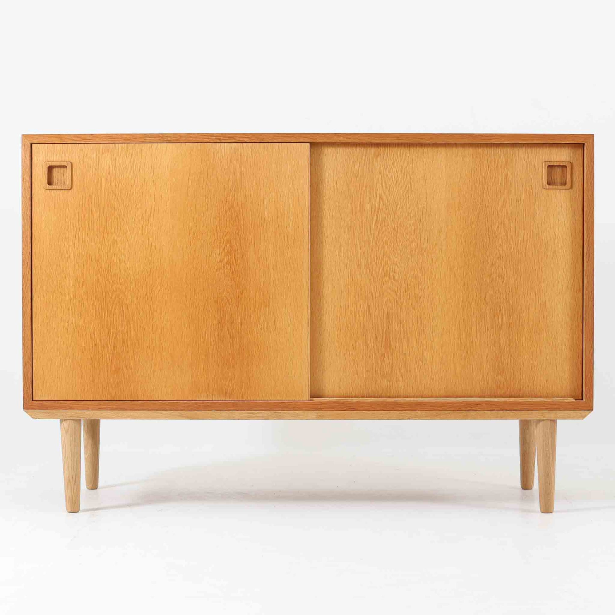 オーク材の美しい木目と柔らかな色味が魅力のこちらのボードは、幅120cmと使い勝手の良いサイズ感で、北欧ビンテージらしい洗練された佇まいが魅力です。内部には可動棚とフェルト付きの浅型引き出しが備えられ、日用品や小物の整理に最適。彫り込み式の取手やテーパードレッグなど、細部にまで配慮された上質な造りが光ります。販売店ラベルとして「Nr. Uttrup Boligmontering」が残されており、当時の流通背景を感じさせる一点物のアイテムです。