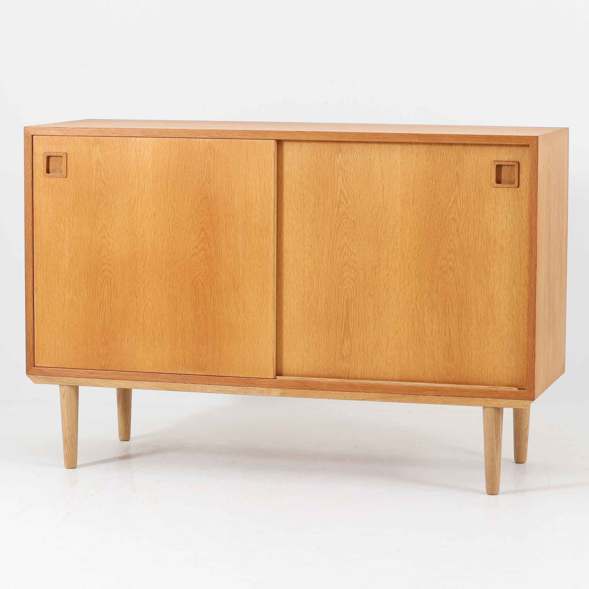 オーク材の美しい木目と柔らかな色味が魅力のこちらのボードは、幅120cmと使い勝手の良いサイズ感で、北欧ビンテージらしい洗練された佇まいが魅力です。内部には可動棚とフェルト付きの浅型引き出しが備えられ、日用品や小物の整理に最適。彫り込み式の取手やテーパードレッグなど、細部にまで配慮された上質な造りが光ります。販売店ラベルとして「Nr. Uttrup Boligmontering」が残されており、当時の流通背景を感じさせる一点物のアイテムです。