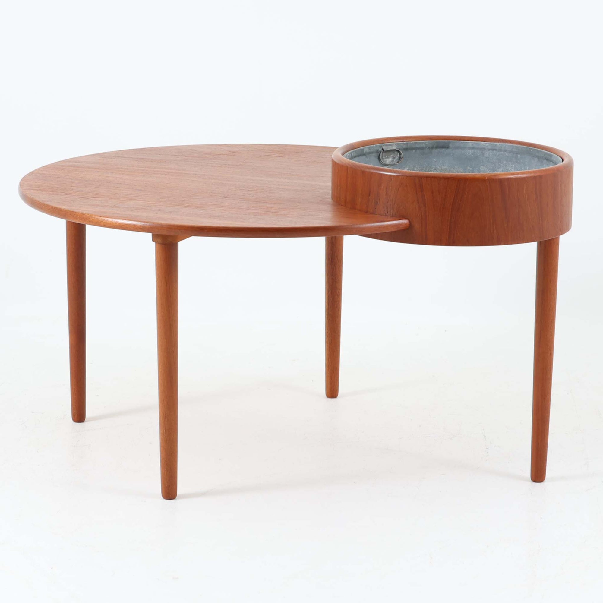 Arne Wahl Iversenがデザインし、Vinde Mobelfabrik社から製造されたユニークなプランター付きセンターテーブルは、チーク材の温かみと実用性を兼ね備えた北欧ビンテージの魅力あふれる一台です。天板の一部にメタル製の植栽スペースが組み込まれており、観葉植物や小物ディスプレイを楽しめる機能的な構造が特徴です。ラウンドフォルムに、スラリと伸びたテーパードレッグが軽やかさを加え、リビング空間に個性と洗練をもたらします。