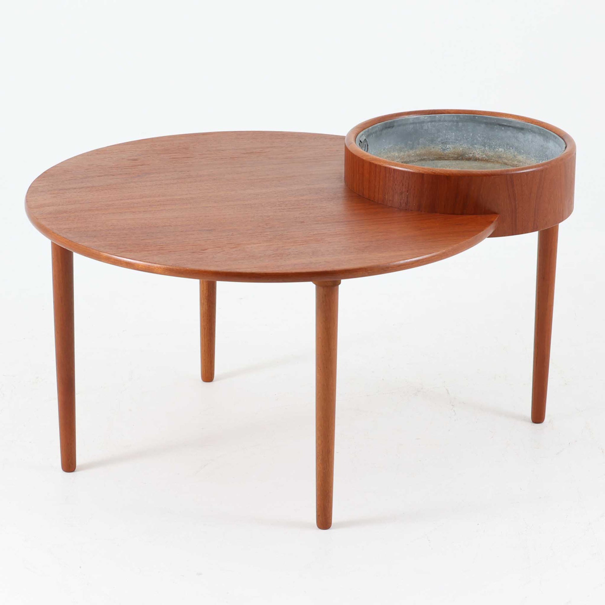 Arne Wahl Iversenがデザインし、Vinde Mobelfabrik社から製造されたユニークなプランター付きセンターテーブルは、チーク材の温かみと実用性を兼ね備えた北欧ビンテージの魅力あふれる一台です。天板の一部にメタル製の植栽スペースが組み込まれており、観葉植物や小物ディスプレイを楽しめる機能的な構造が特徴です。ラウンドフォルムに、スラリと伸びたテーパードレッグが軽やかさを加え、リビング空間に個性と洗練をもたらします。