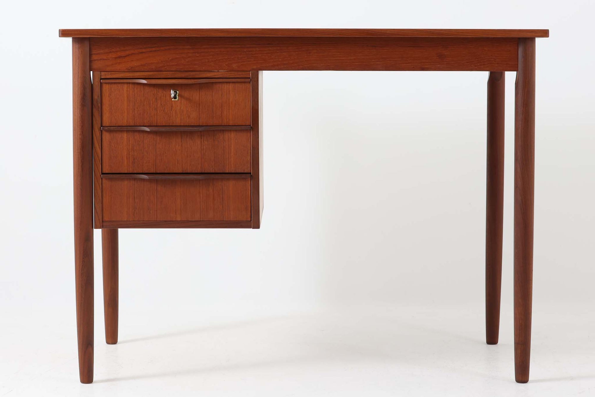 シンプルで洗練された佇まいが魅力のこちらの片袖デスクは、上質なチーク材を用いた北欧ビンテージ家具です。丸みを帯びたテーパードレッグや、緩やかにカーブした引き出しの取っ手が、温もりと職人技を感じさせるディテールとなっています。引き出しは3段構成で収納力があり、鍵付きの上段は大切な書類の保管にも最適です。コンパクトながら実用性に優れており、ワークデスクやドレッサー代わりとしてもおすすめできる逸品です。経年変化による木肌の風合いもビンテージならではの魅力で、空間に落ち着きと品格を与えてくれます。