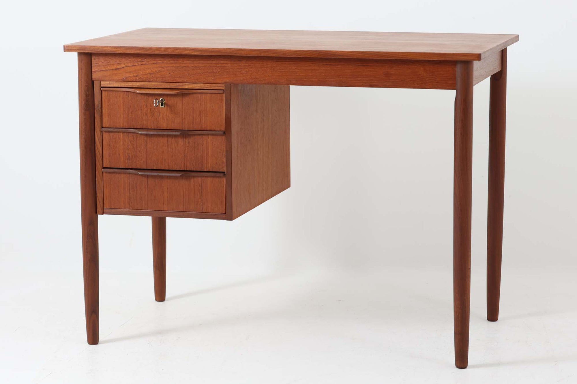 シンプルで洗練された佇まいが魅力のこちらの片袖デスクは、上質なチーク材を用いた北欧ビンテージ家具です。丸みを帯びたテーパードレッグや、緩やかにカーブした引き出しの取っ手が、温もりと職人技を感じさせるディテールとなっています。引き出しは3段構成で収納力があり、鍵付きの上段は大切な書類の保管にも最適です。コンパクトながら実用性に優れており、ワークデスクやドレッサー代わりとしてもおすすめできる逸品です。経年変化による木肌の風合いもビンテージならではの魅力で、空間に落ち着きと品格を与えてくれます。