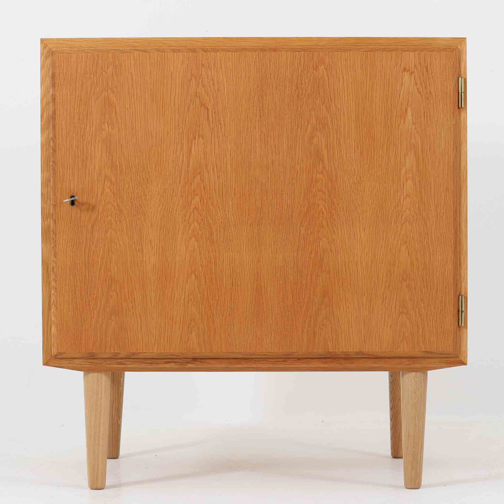 Poul Hundevadがデザインし、Hundevad & Co社から製造されたこちらのキャビネットは、上質なオーク材を用いた小ぶりな北欧ビンテージ品で、すっきりとした面構えと繊細な脚部が印象的な一台です。鍵付きの開き戸を備え、内部には棚板が設けられており、収納家具としての実用性に加え、空間にナチュラルで落ち着いた佇まいをもたらします。なお、脚部は後年に交換されている可能性がありますが、全体の雰囲気を損なわない自然な仕上がりです。