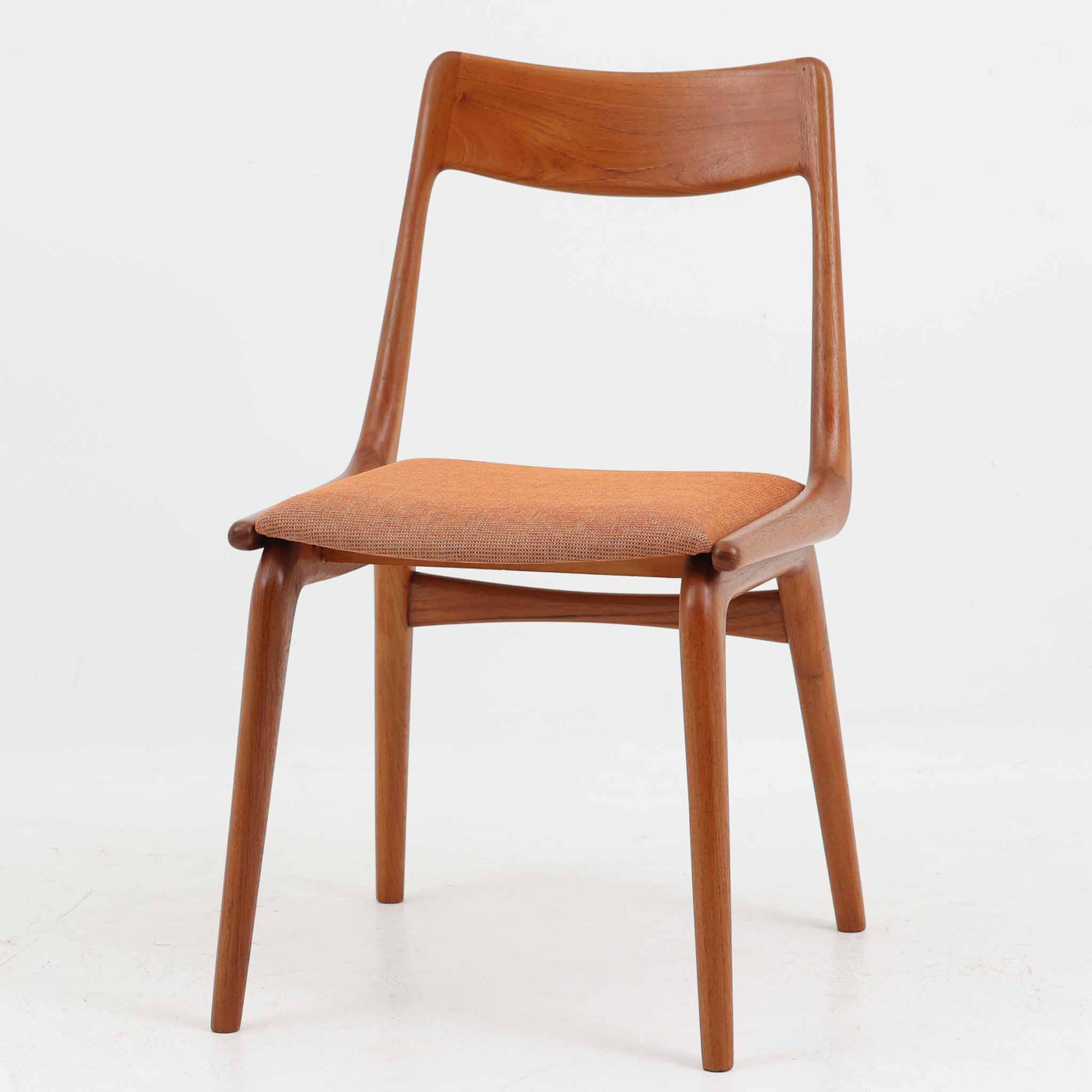 Alfred Christensen（アルフレッド・クリステンセン）によるデザインで、Slagelse Mobelvaerk社から発表されたブーメランチェアです。背から後脚にかけて滑らかに繋がるチーク材の曲線が美しく、丹念な削り出しによる立体的な造形が印象的です。オレンジ系の張地が温かみを添え、北欧らしい明るい雰囲気を演出します。軽やかなフォルムながらしっかりとした安定感があり、ダイニングチェアとしてはもちろん、デスクチェアとしてもお使いいただけます。経年により深みを増した木肌が、ビンテージならではの風格を感じさせる一脚です。