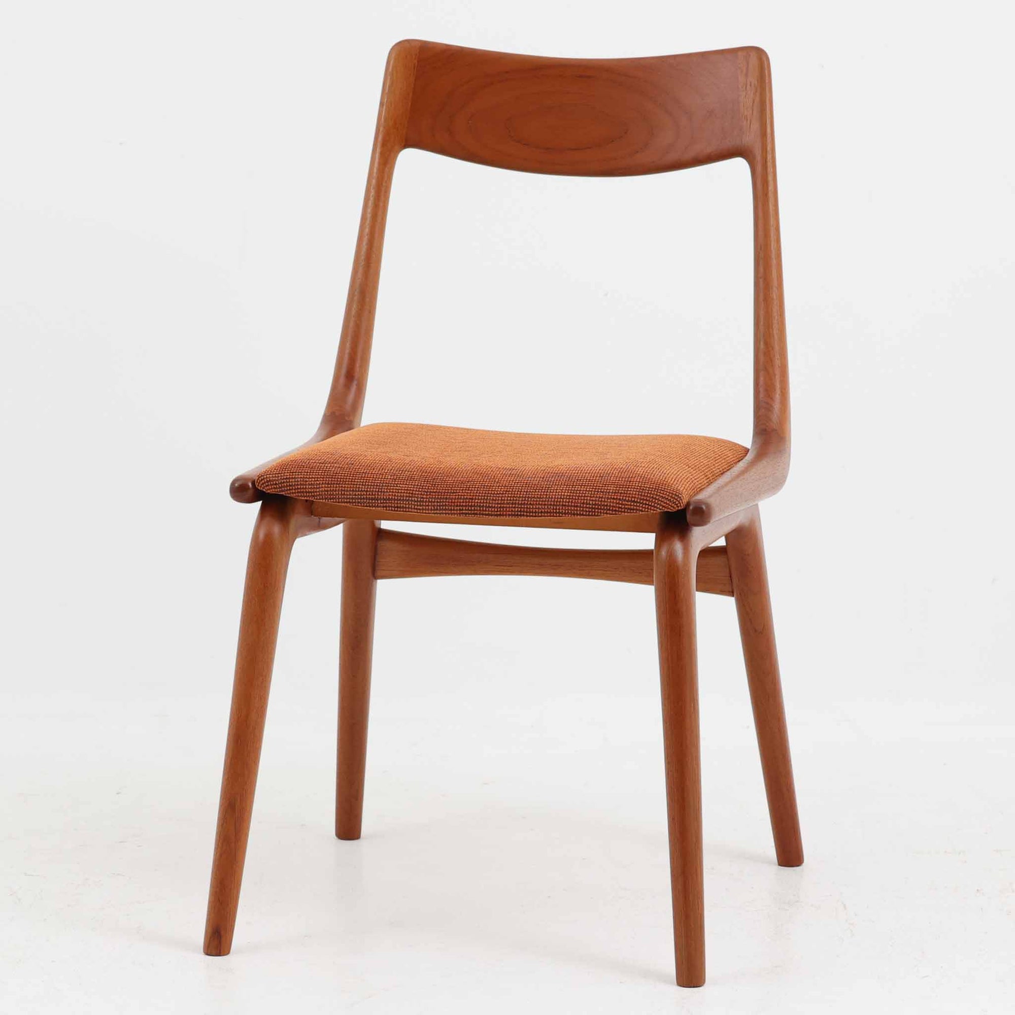 Alfred Christensen（アルフレッド・クリステンセン）によるデザインで、Slagelse Mobelvaerk社から発表されたブーメランチェアです。背から後脚にかけて滑らかに繋がるチーク材の曲線が美しく、丹念な削り出しによる立体的な造形が印象的です。オレンジ系の張地が温かみを添え、北欧らしい明るい雰囲気を演出します。軽やかなフォルムながらしっかりとした安定感があり、ダイニングチェアとしてはもちろん、デスクチェアとしてもお使いいただけます。経年により深みを増した木肌が、ビンテージならではの風格を感じさせる一脚です。