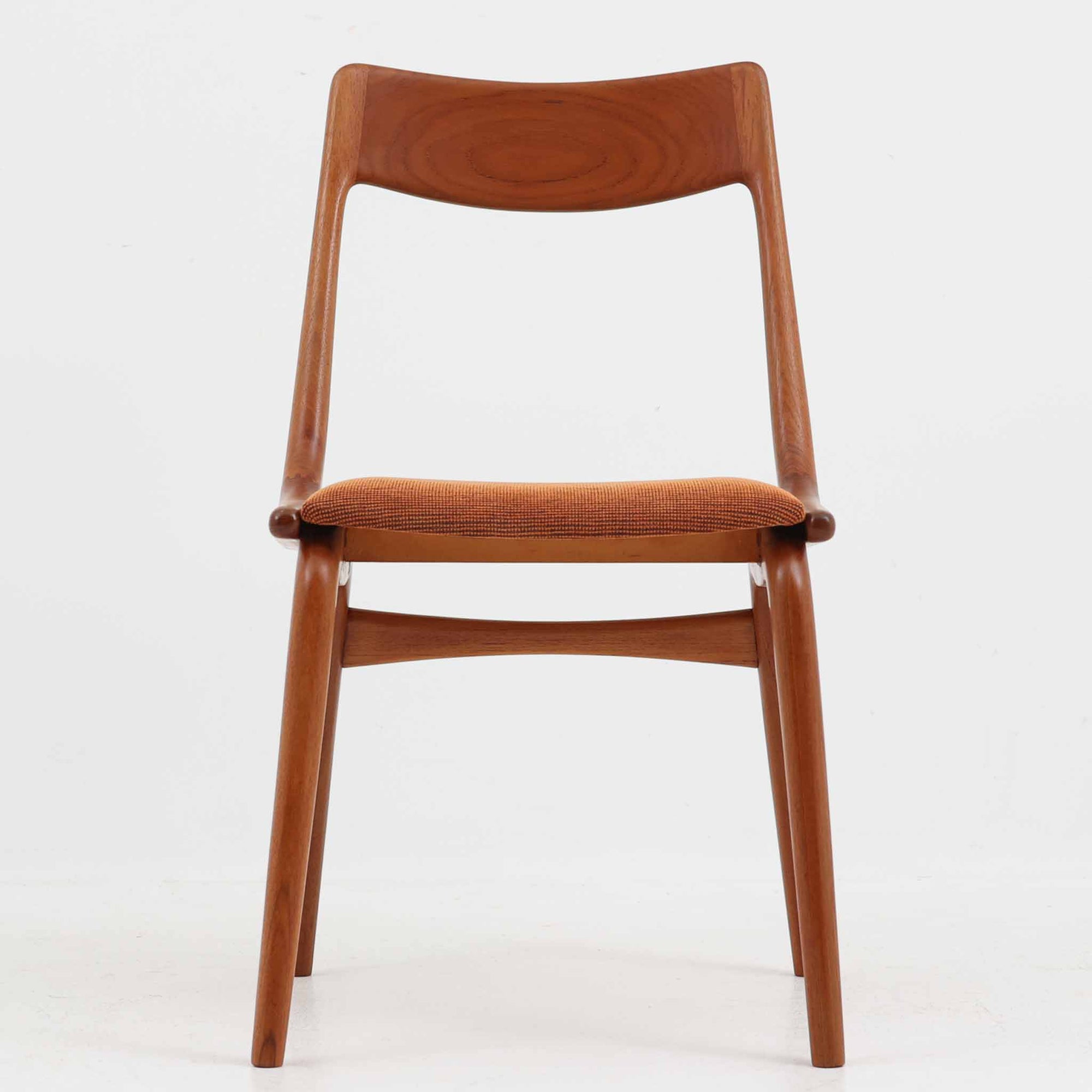 Alfred Christensen（アルフレッド・クリステンセン）によるデザインで、Slagelse Mobelvaerk社から発表されたブーメランチェアです。背から後脚にかけて滑らかに繋がるチーク材の曲線が美しく、丹念な削り出しによる立体的な造形が印象的です。オレンジ系の張地が温かみを添え、北欧らしい明るい雰囲気を演出します。軽やかなフォルムながらしっかりとした安定感があり、ダイニングチェアとしてはもちろん、デスクチェアとしてもお使いいただけます。経年により深みを増した木肌が、ビンテージならではの風格を感じさせる一脚です。
