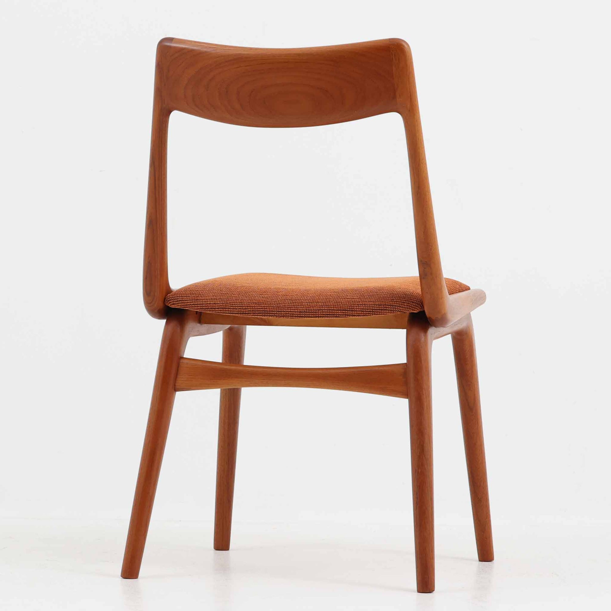 Alfred Christensen（アルフレッド・クリステンセン）によるデザインで、Slagelse Mobelvaerk社から発表されたブーメランチェアです。背から後脚にかけて滑らかに繋がるチーク材の曲線が美しく、丹念な削り出しによる立体的な造形が印象的です。オレンジ系の張地が温かみを添え、北欧らしい明るい雰囲気を演出します。軽やかなフォルムながらしっかりとした安定感があり、ダイニングチェアとしてはもちろん、デスクチェアとしてもお使いいただけます。経年により深みを増した木肌が、ビンテージならではの風格を感じさせる一脚です。