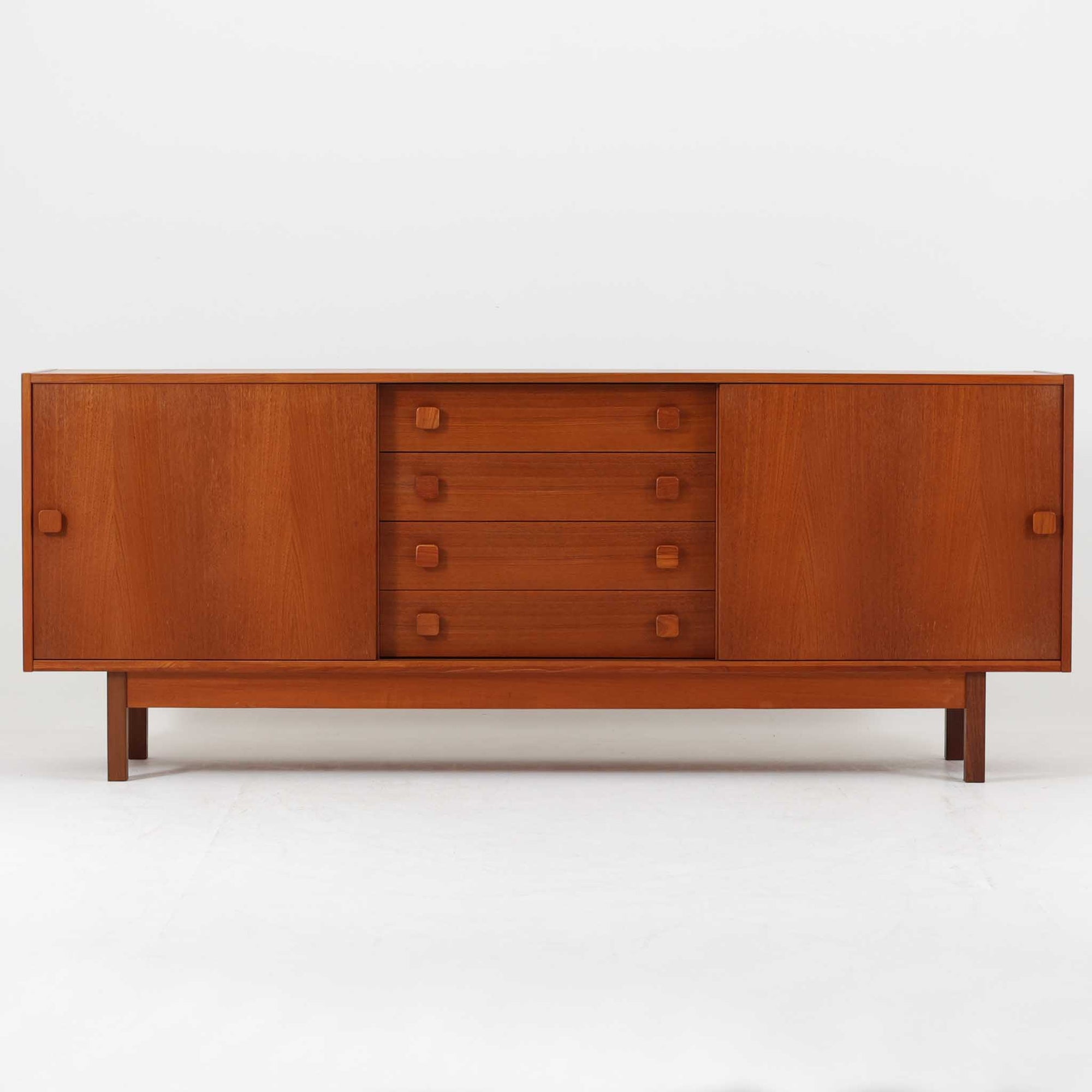 Domino Mobler社製の幅182cmのボードは、上質なチーク材を用いた美しい木目と、左右の開き戸と中央の引き出しという機能的な構成が魅力の北欧ビンテージ家具です。丸みのあるスクエア取手や脚部のすっきりとしたラインが、端正なフォルムを引き立てつつ温かみも感じさせます。収納力にも優れ、リビングやダイニングで食器や日用品を収めるサイドボードとしてはもちろん、テレビボードとしても活躍する汎用性の高い一台です。