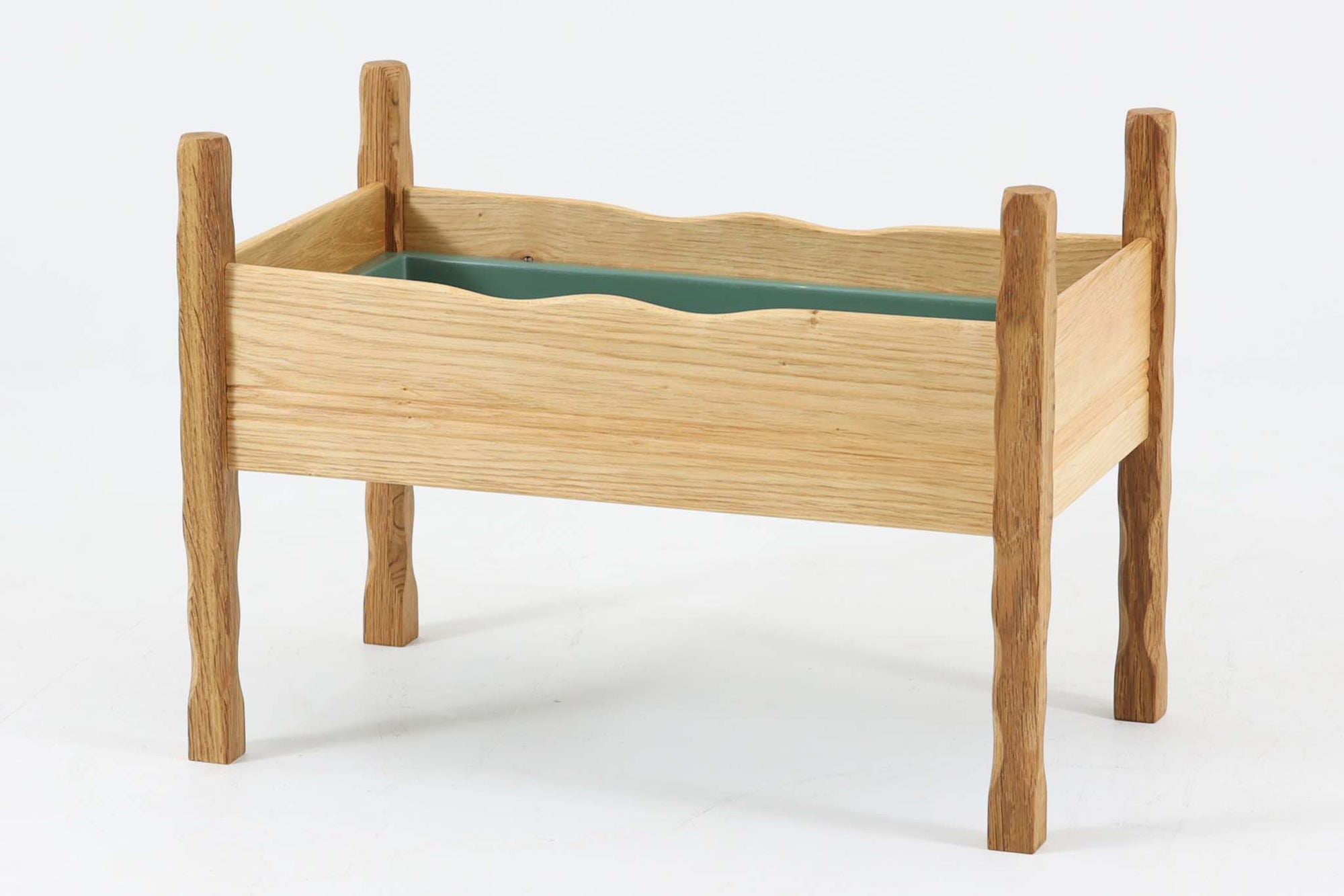 デンマーク製のビンテージプランターです。オーク材を使用し、自然な木目と素材感を活かしたデザインが特徴的です。脚部は不規則な表情を持つ無垢材を使用し、オーガニックな印象を演出。本体は美しい木目のオーク材で構成され、内部には緑色のトレイが備え付けられています。波打つような上部のラインは、無機質になりがちなプランターに優しい表情を与えています。北欧デザインらしい、自然との調和を意識した佇まいは、観葉植物や季節の花々を引き立てる上質なプランターとして、現代のインテリアにも自然に溶け込むのではないでしょうか。