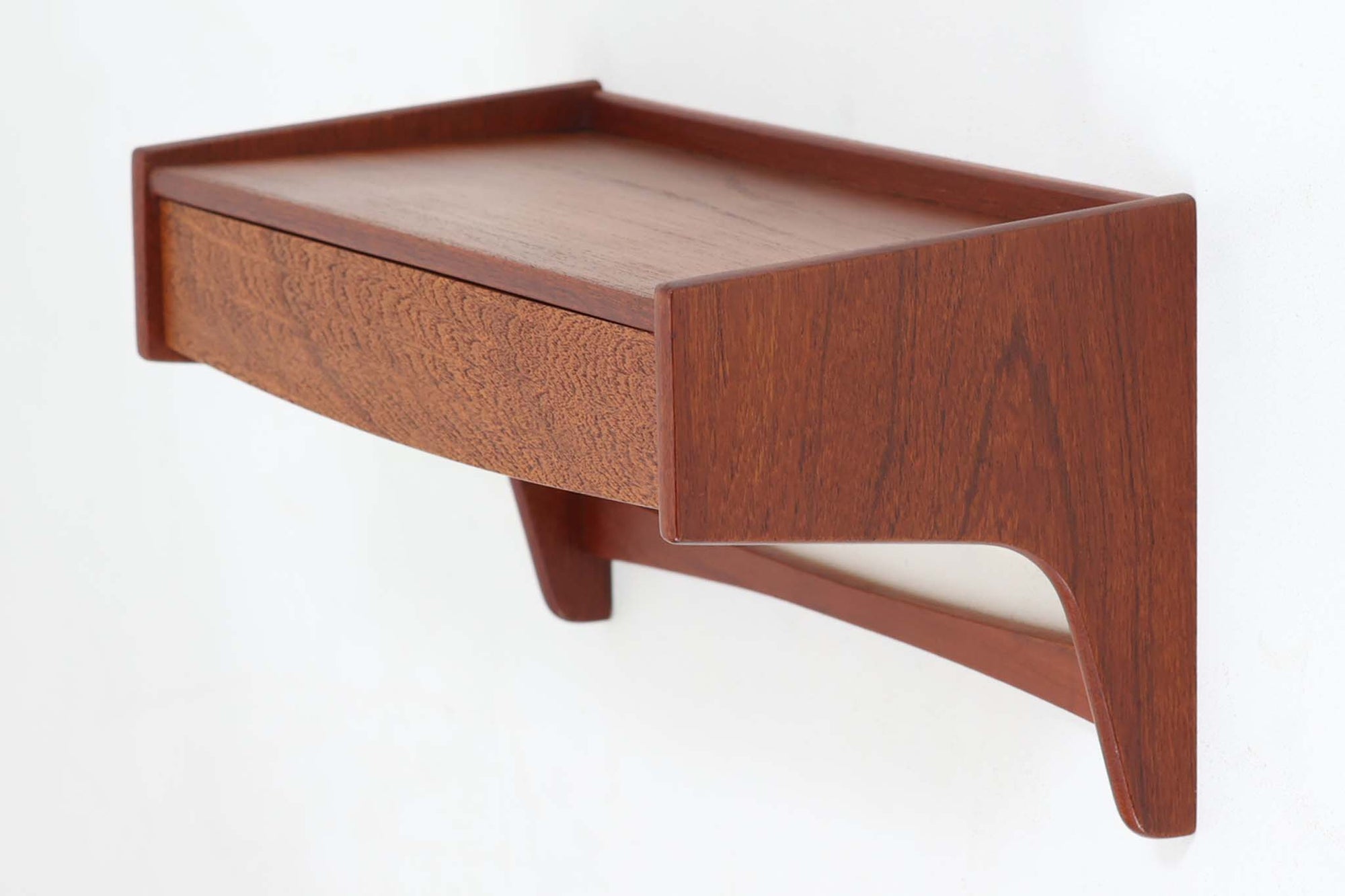デンマーク製のビンテージ壁掛けシェルフです。上質なチーク材を使用し、美しい木目と深みのある色合いが特徴的です。前面にはドロワーを配置し、小物類の収納に便利な機能性を備えています。天板部分は縁立ちのデザインで、装飾品や小物を安全に飾ることができます。サイドの支柱は緩やかなカーブを描き、北欧モダンならではの優美なフォルムを演出。コンパクトながら存在感のあるデザインは、玄関やリビングなど様々な空間で活躍します。シンプルな中にも確かな職人技が感じられる、1960年代を代表する北欧家具の逸品です。