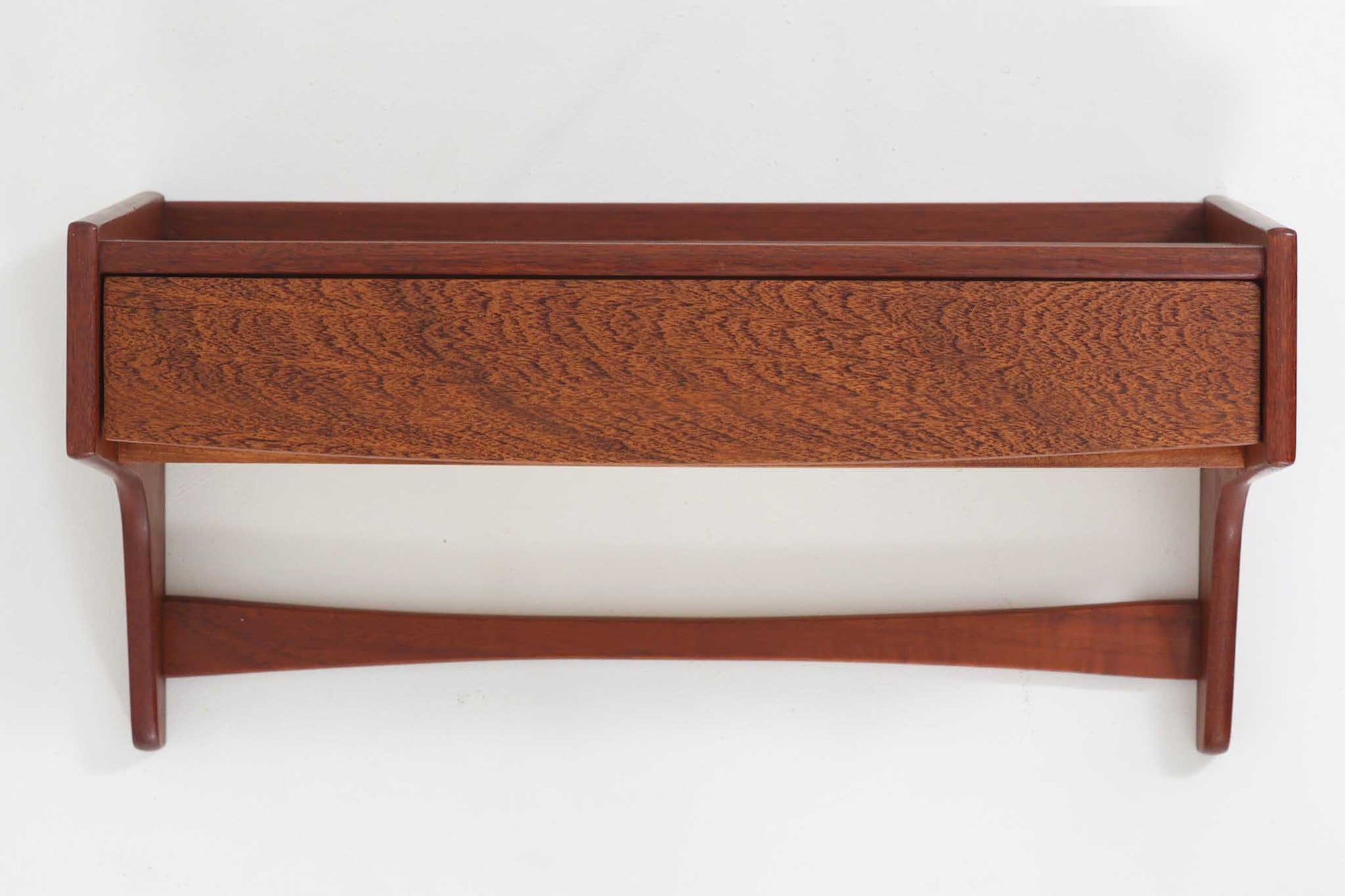 デンマーク製のビンテージ壁掛けシェルフです。上質なチーク材を使用し、美しい木目と深みのある色合いが特徴的です。前面にはドロワーを配置し、小物類の収納に便利な機能性を備えています。天板部分は縁立ちのデザインで、装飾品や小物を安全に飾ることができます。サイドの支柱は緩やかなカーブを描き、北欧モダンならではの優美なフォルムを演出。コンパクトながら存在感のあるデザインは、玄関やリビングなど様々な空間で活躍します。シンプルな中にも確かな職人技が感じられる、1960年代を代表する北欧家具の逸品です。