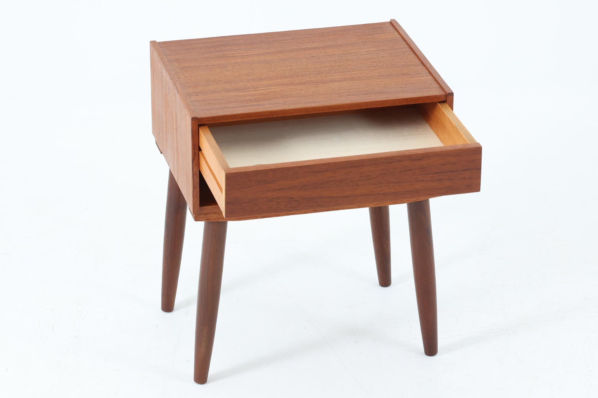 デンマークで製造されたヴィンテージのサイドチェスト。温もりのあるチーク材を用いた本体に、先細りの丸脚を組み合わせた軽やかな佇まいが魅力です。引き出し1杯に加え、下部にはオープンスペースを備えており、リモコンや文庫本などをすぐに取り出せる実用的な構造。天板や側面にはすっきりとした面取りが施され、シンプルなデザインの中に丁寧な仕事が感じられます。北欧らしいあたたかみと実用性を兼ね備えた一台。ベッドサイドはもちろん、リビングや玄関先など、暮らしのさまざまな場面で活躍します。