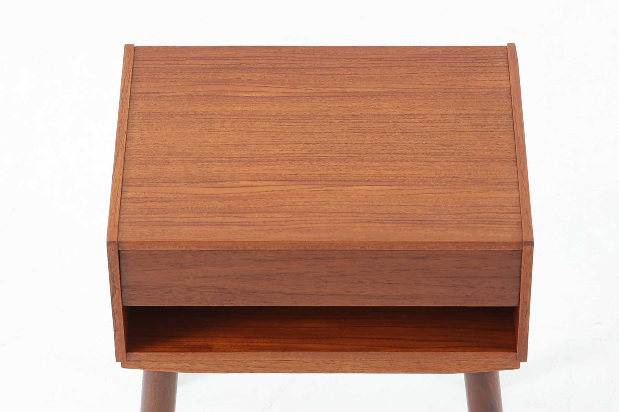 デンマークで製造されたヴィンテージのサイドチェスト。温もりのあるチーク材を用いた本体に、先細りの丸脚を組み合わせた軽やかな佇まいが魅力です。引き出し1杯に加え、下部にはオープンスペースを備えており、リモコンや文庫本などをすぐに取り出せる実用的な構造。天板や側面にはすっきりとした面取りが施され、シンプルなデザインの中に丁寧な仕事が感じられます。北欧らしいあたたかみと実用性を兼ね備えた一台。ベッドサイドはもちろん、リビングや玄関先など、暮らしのさまざまな場面で活躍します。