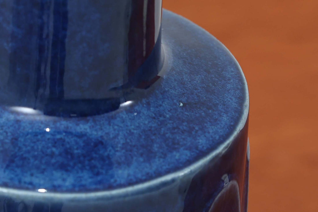 デンマークの陶器ブランドDesiree（デシレ）によって制作されたヴィンテージのテーブルランプ。艶やかな深いブルーの釉薬に、楕円形のレリーフがリズミカルに並ぶ印象的なデザインが魅力です。フォルムはシンプルながらも彫刻的で、北欧陶器ならではの温かみと落ち着きを感じさせます。ベース底部には「Desiree Stentoj – Denmark」の刻印と品番「2010」が施されています。シェードには新品のリネン製シェードを合わせ、光をやわらかく拡散。ベッドサイドやリビングのアクセントとして、空間に静かな存在感を添える一灯です。