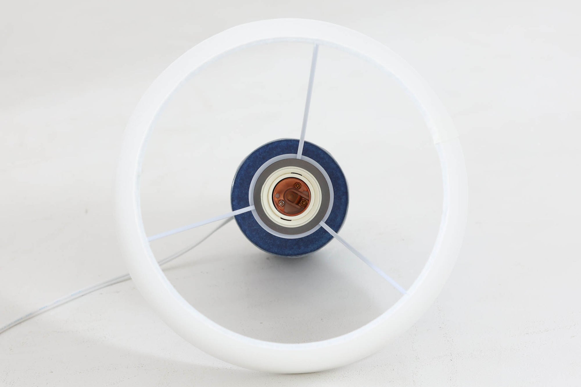 デンマークの陶器ブランドDesiree（デシレ）によって制作されたヴィンテージのテーブルランプ。艶やかな深いブルーの釉薬に、楕円形のレリーフがリズミカルに並ぶ印象的なデザインが魅力です。フォルムはシンプルながらも彫刻的で、北欧陶器ならではの温かみと落ち着きを感じさせます。ベース底部には「Desiree Stentoj – Denmark」の刻印と品番「2010」が施されています。シェードには新品のリネン製シェードを合わせ、光をやわらかく拡散。ベッドサイドやリビングのアクセントとして、空間に静かな存在感を添える一灯です。