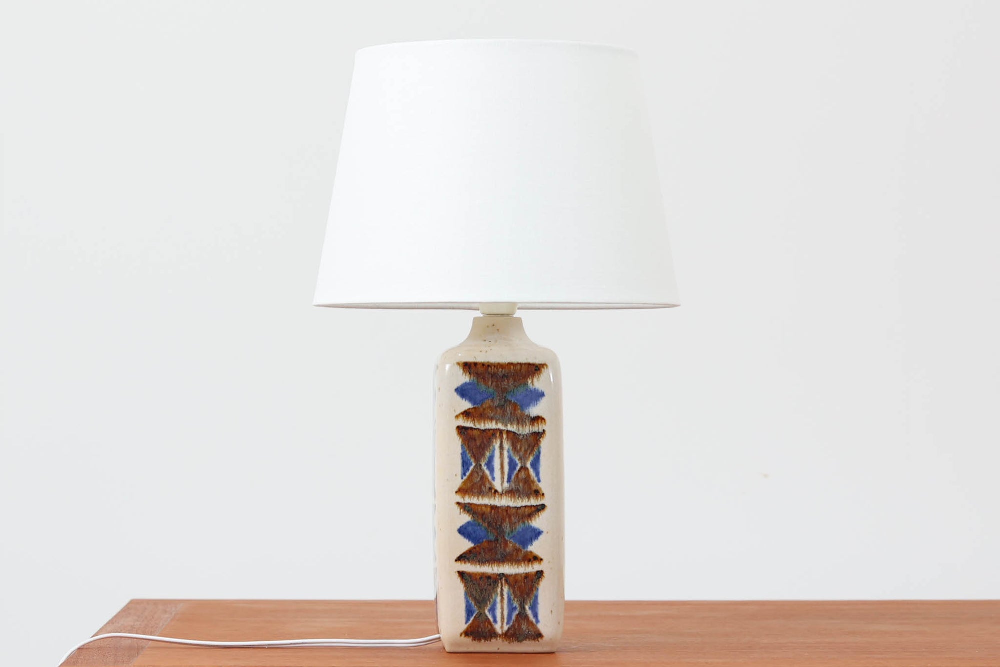 デンマークの名窯michael Andersen & Sønによるテーブルランプ。アイボリートーンの陶器ボディにブルーやブラウンの幾何学模様が手描きであしらわれた美しい一点。光沢のある釉薬の表情も魅力的です。シェードは新品のリネン製に交換済み。