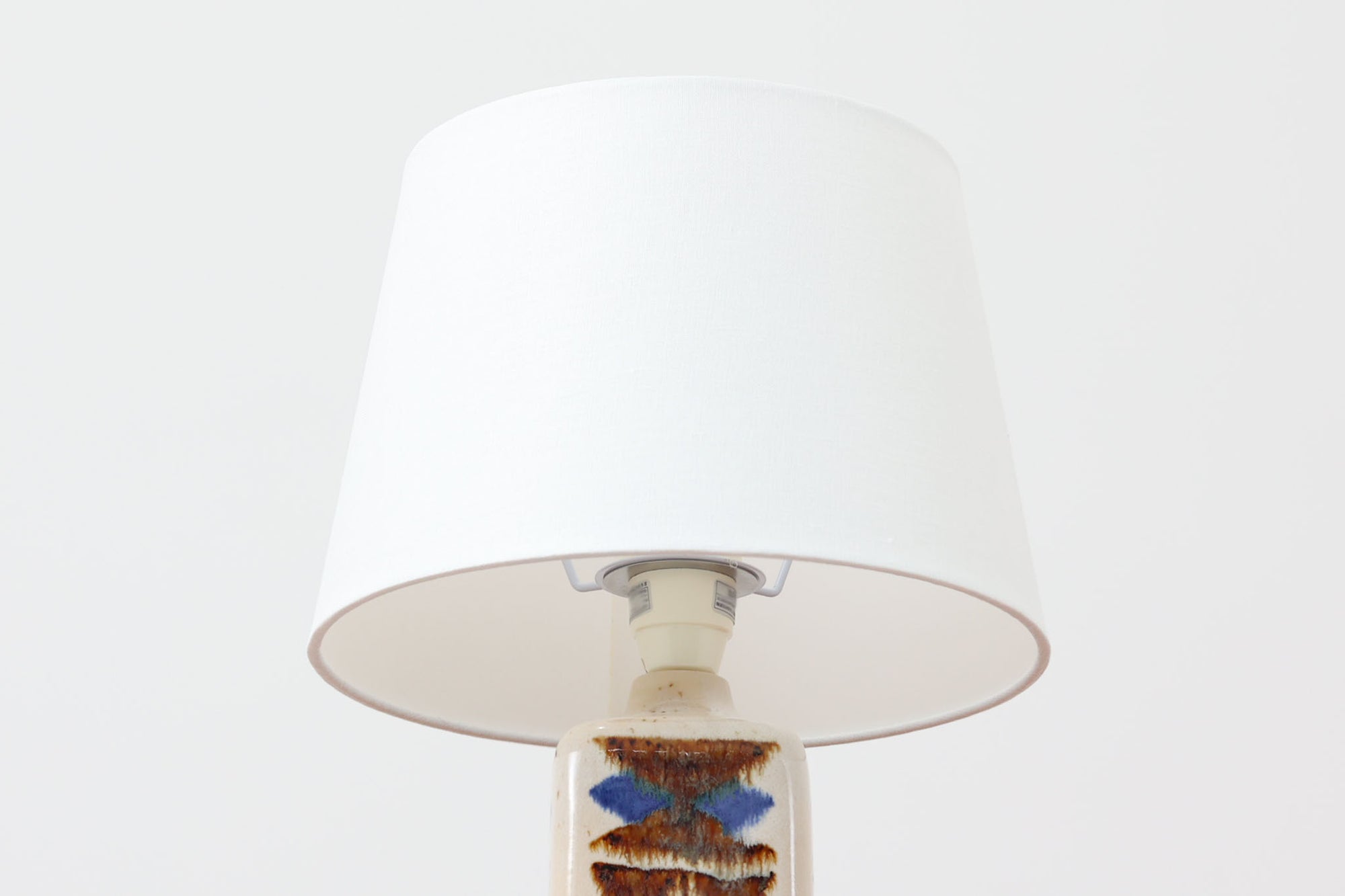 デンマークの名窯michael Andersen &amp; Sønによるテーブルランプ。アイボリートーンの陶器ボディにブルーやブラウンの幾何学模様が手描きであしらわれた美しい一点。光沢のある釉薬の表情も魅力的です。シェードは新品のリネン製に交換済み。