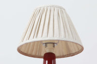 デンマークの照明ブランドLe Klint（レ・クリント）のテーブルランプで、デザイナーはOle Boggild（オーレ・ボギル）。艶やかなレッドの釉薬が美しく、ふっくらと丸みを帯びたフォルムが愛らしくも上品な印象を与えます。シェードはLe Klint社製ではありませんが、新品のリネン製プリーツシェードを合わせており、クラシカルな佇まいと柔らかな光を演出します。北欧らしい温かみと洗練された存在感を持ち、ベッドサイドやリビングのアクセントとして取り入れやすい一灯です。