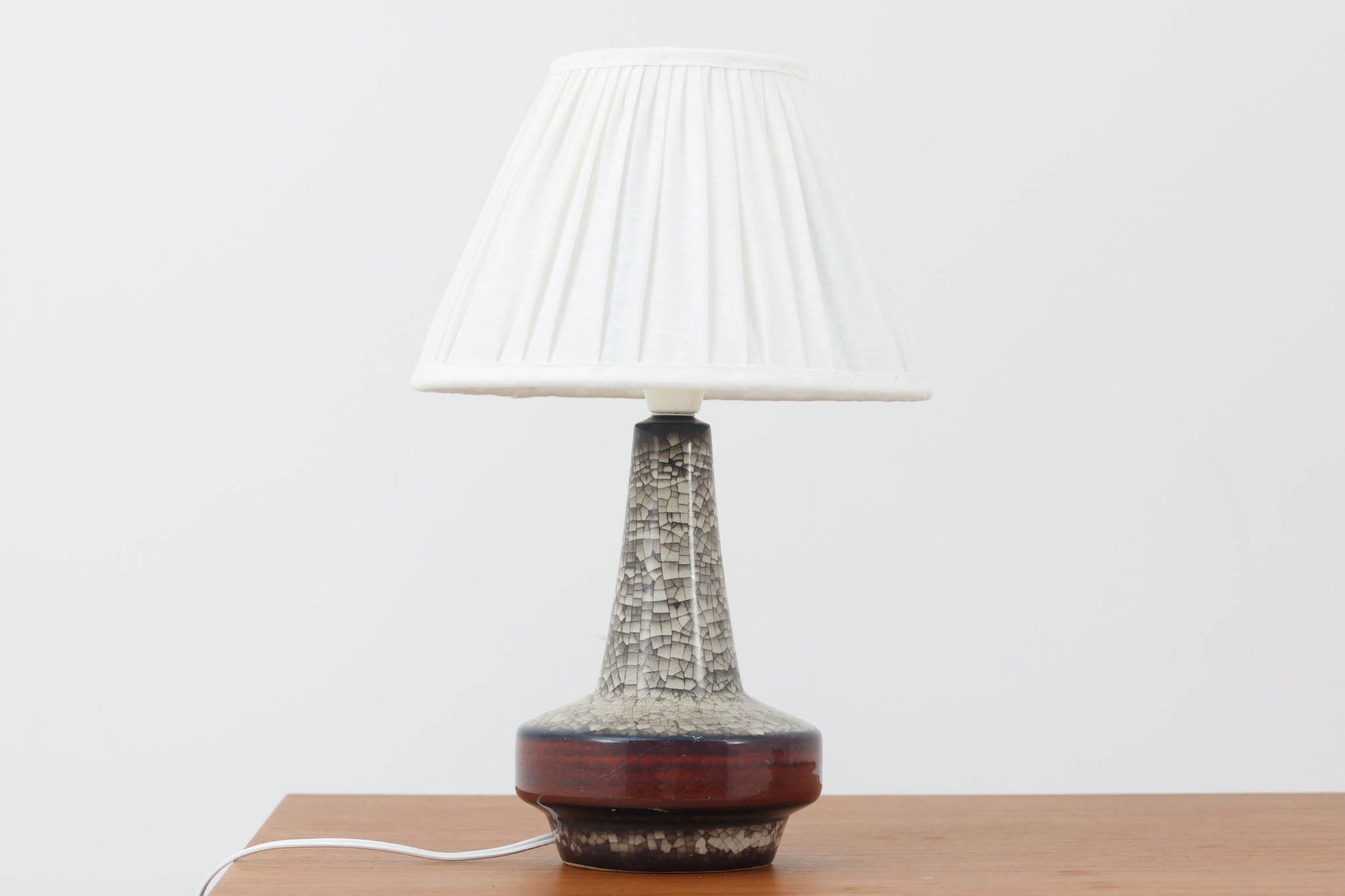 デンマーク・ボーンホルム島の老舗陶器メーカー、michael Andersen & Sonによるテーブルランプ。細やかな貫入模様と深みのある釉薬の色合いが特徴で、ベース部分は温かみのあるクラフト感を漂わせています。シェードは新品のリネン製で、やさしく光を拡散し、空間に柔らかな雰囲気をもたらします。北欧ヴィンテージらしい造形美と素材感を楽しめる一点です。