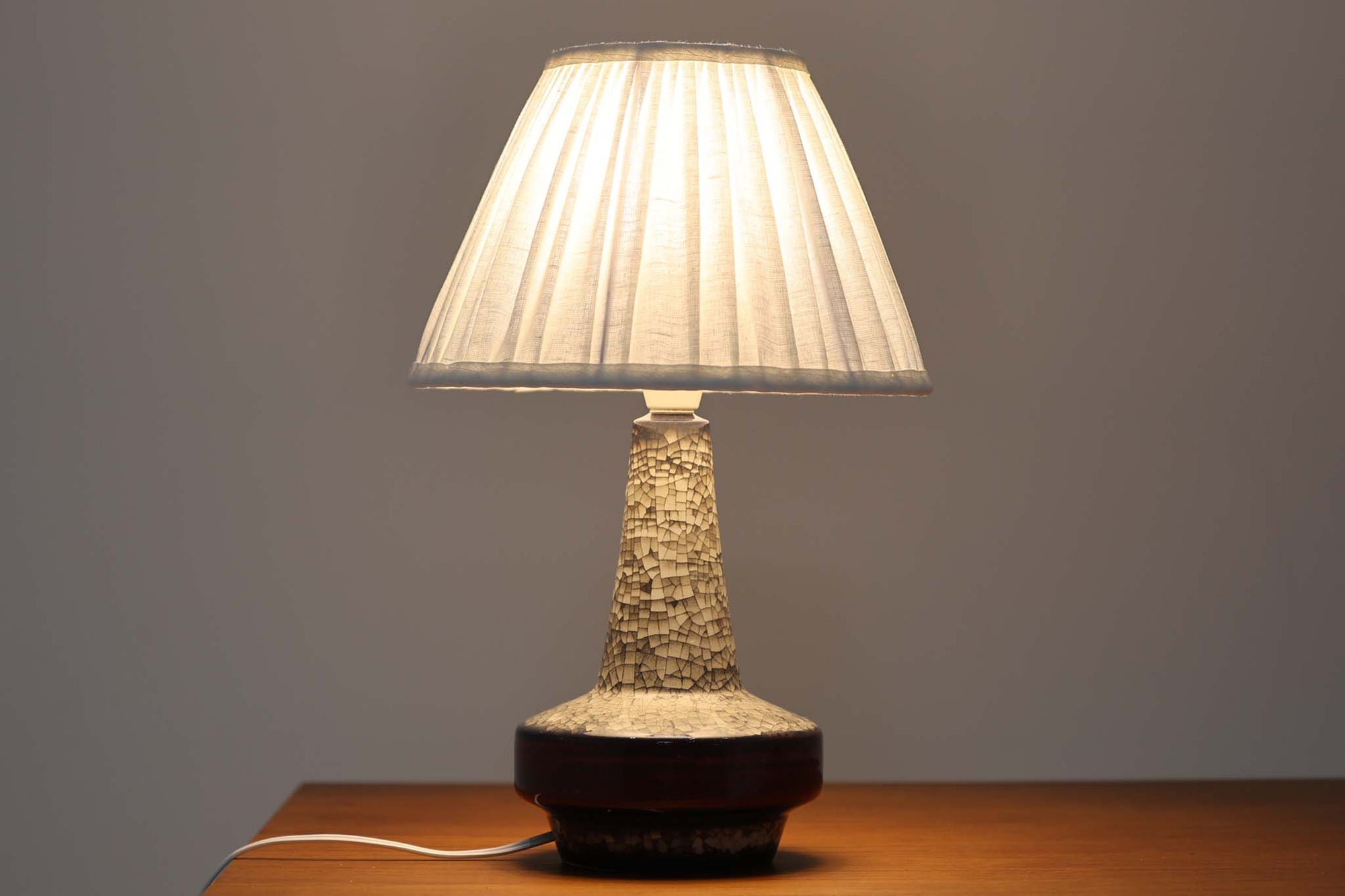 デンマーク・ボーンホルム島の老舗陶器メーカー、michael Andersen & Sonによるテーブルランプ。細やかな貫入模様と深みのある釉薬の色合いが特徴で、ベース部分は温かみのあるクラフト感を漂わせています。シェードは新品のリネン製で、やさしく光を拡散し、空間に柔らかな雰囲気をもたらします。北欧ヴィンテージらしい造形美と素材感を楽しめる一点です。