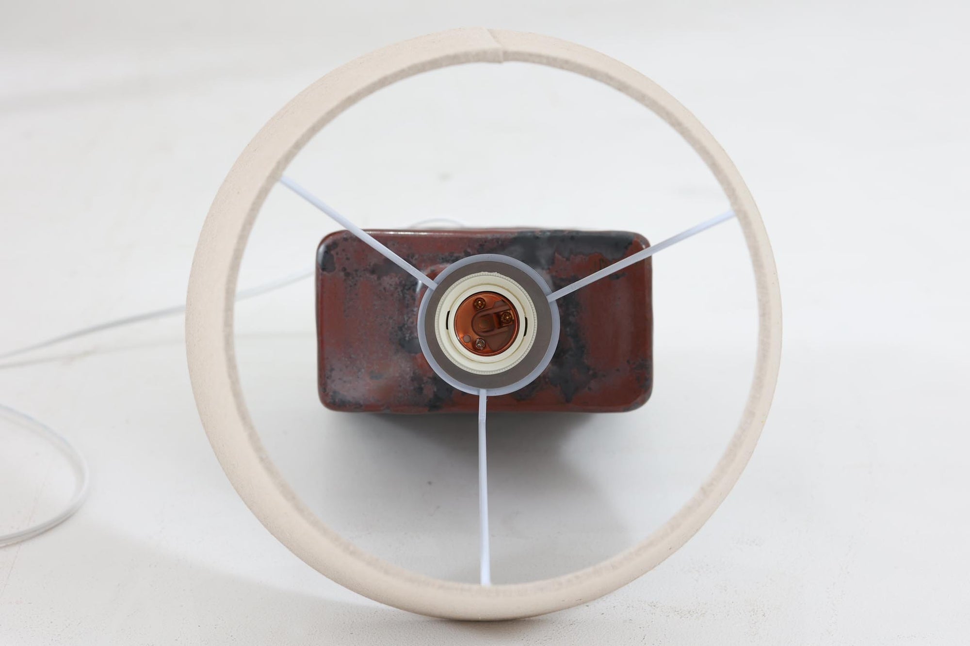 デンマークの陶器ブランドDesiree（デシレ）によって制作されたヴィンテージのテーブルランプ。赤褐色と黒の釉薬が溶け合うように流れ、唯一無二の表情を生み出しています。スクエア型のフォルムに施された厚みのある釉薬の質感は、重厚感と美しさを兼ね備えており、北欧陶器らしい存在感を感じさせます。底部には「Desiree Stentoj – Denmark」の刻印と品番「2071」が見られます。シェードには新品のリネン製を合わせ、やわらかな光が落ち着いた雰囲気を演出します。ヴィンテージらしい個性と静かな力強さを持った一点です。