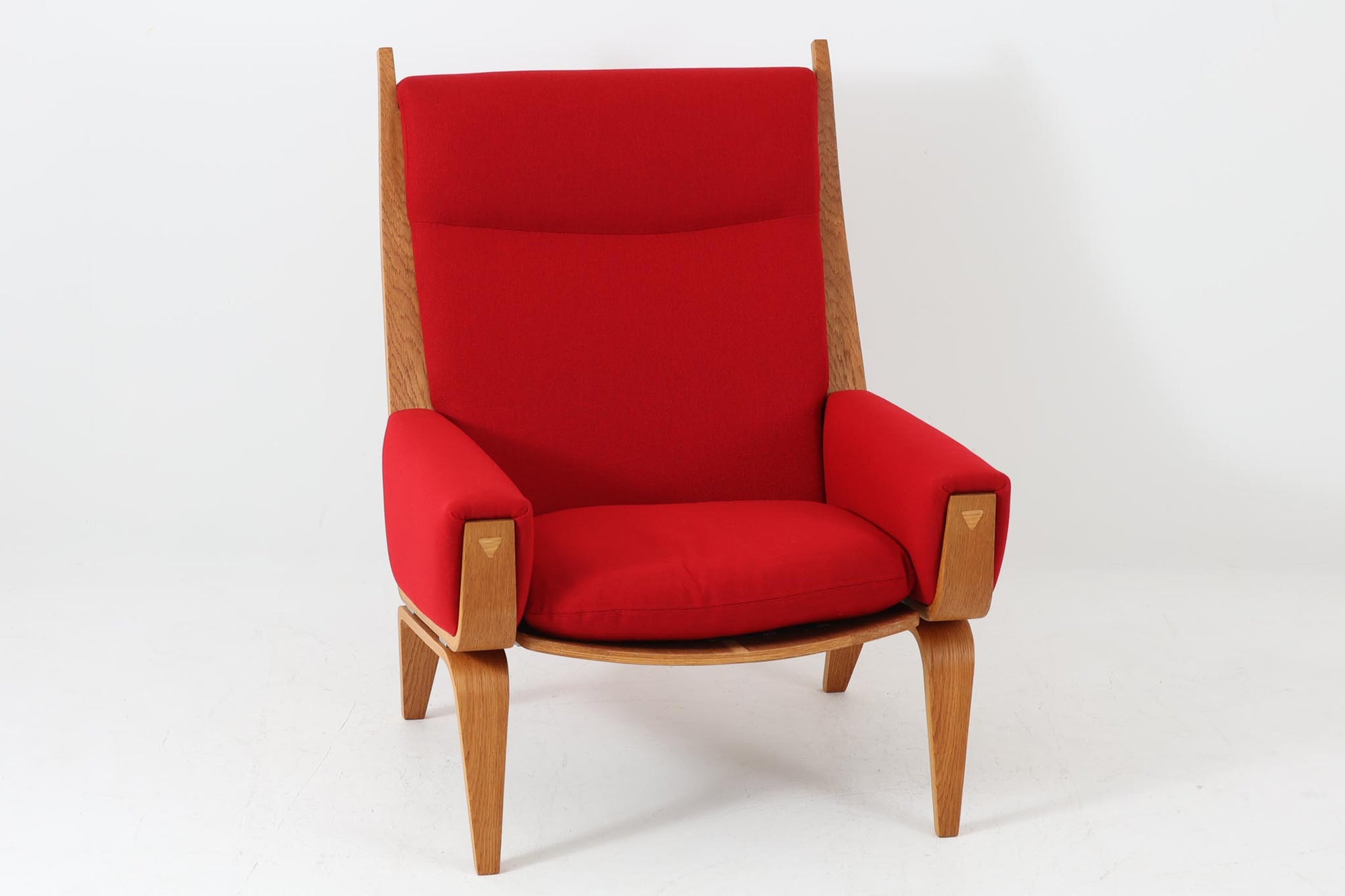 Hans J. Wegner（ハンス・J・ウェグナー）が1960年代にデザインし、Getama（ゲタマ）社によって製造されたGE501Aモデルのハイバックシングルソファ。当時としては珍しく、フレームにプライウッドが使用されています。フレームには堅牢で美しい木目を持つオーク材を使用し、直線と曲線が融合した造形が北欧家具らしい洗練された印象を与えます。張地には鮮やかな赤のファブリックを使用し、空間にアクセントを添えると同時に、快適性と耐久性も兼ね備えた仕上がりです。ヴィンテージならではの存在感と高い実用性を兼ね備えた一脚として、リビングや読書スペースに最適です。