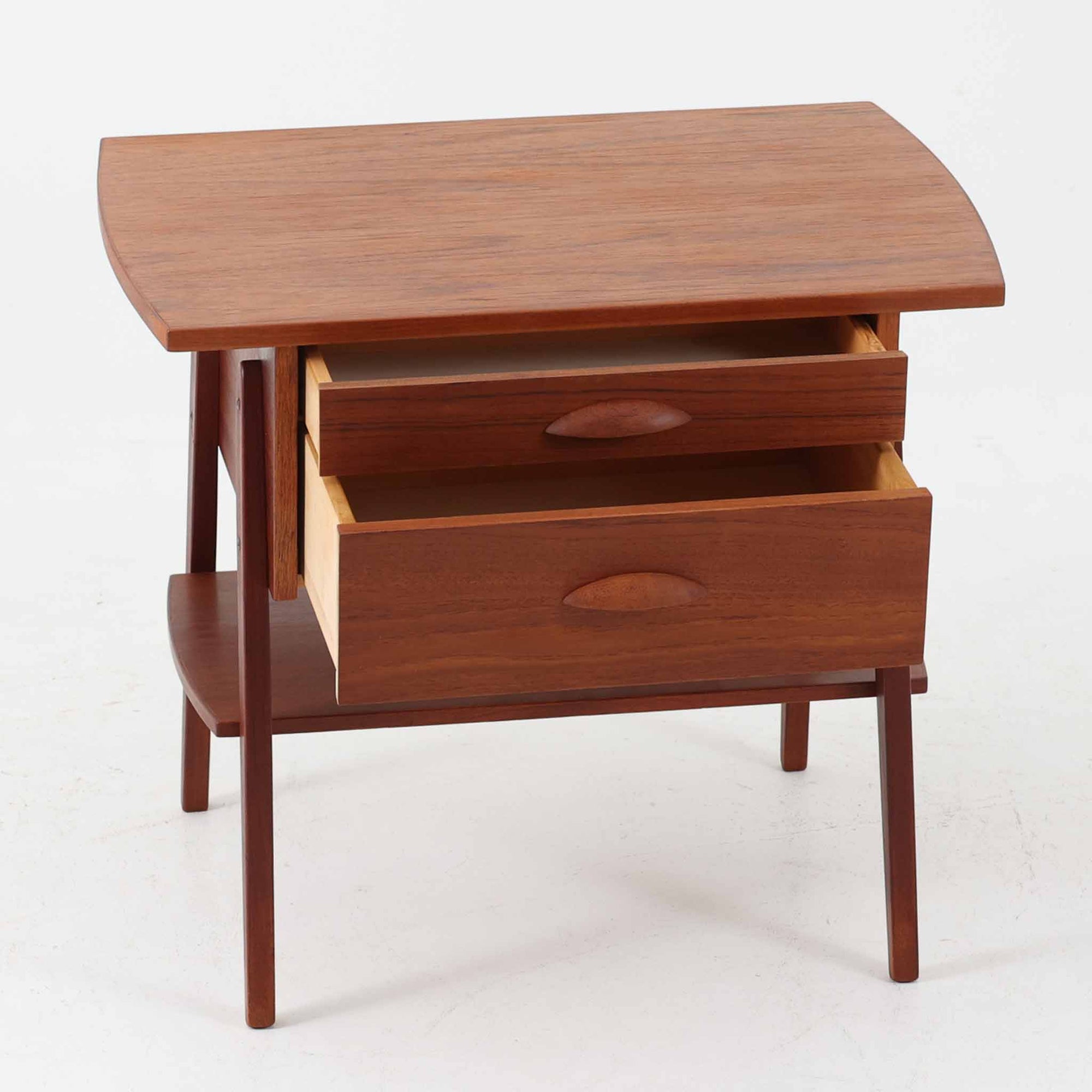 チーク材を用いたこちらの2段チェストは、緩やかにカーブした天板と舟形の引き手が特徴的な北欧ビンテージ家具です。幅64cmとコンパクトながらも引き出し2杯と下部の棚板を備え、収納力とディスプレイ性を兼ね備えています。テーパー脚が軽やかな印象を与え、ベッドサイドやリビングのサイドテーブルとしても活躍。年月を経た木肌の温かみが、空間に落ち着きと味わい深い存在感をもたらす一品です。
