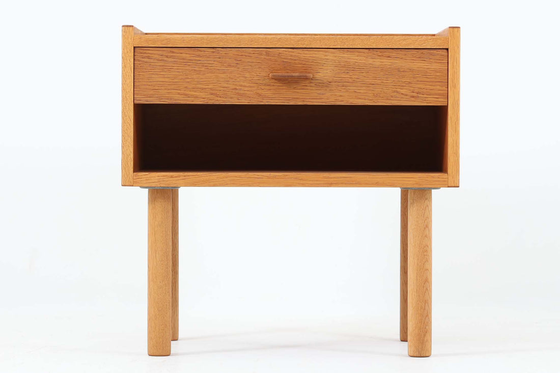 デンマークを代表する家具デザイナー、Hans J. Wegner（ハンス・J・ウェグナー）によってデザインされた、Ry mobler社製のビンテージサイドテーブルです。素材にはあたたかみのあるオーク材が用いられており、北欧らしいシンプルかつ機能的な美しさが感じられます。天板は縁に立ち上がりがあり、物が転がり落ちにくい仕様。引き出しとオープンスペースが組み合わされた実用的な構造で、ベッドサイドやソファ横、玄関周りなど様々なシーンで活躍します。無駄のないデザインと丸脚の柔らかな佇まいが魅力で、ウェグナーデザインならではのバランス感が光る一台です。