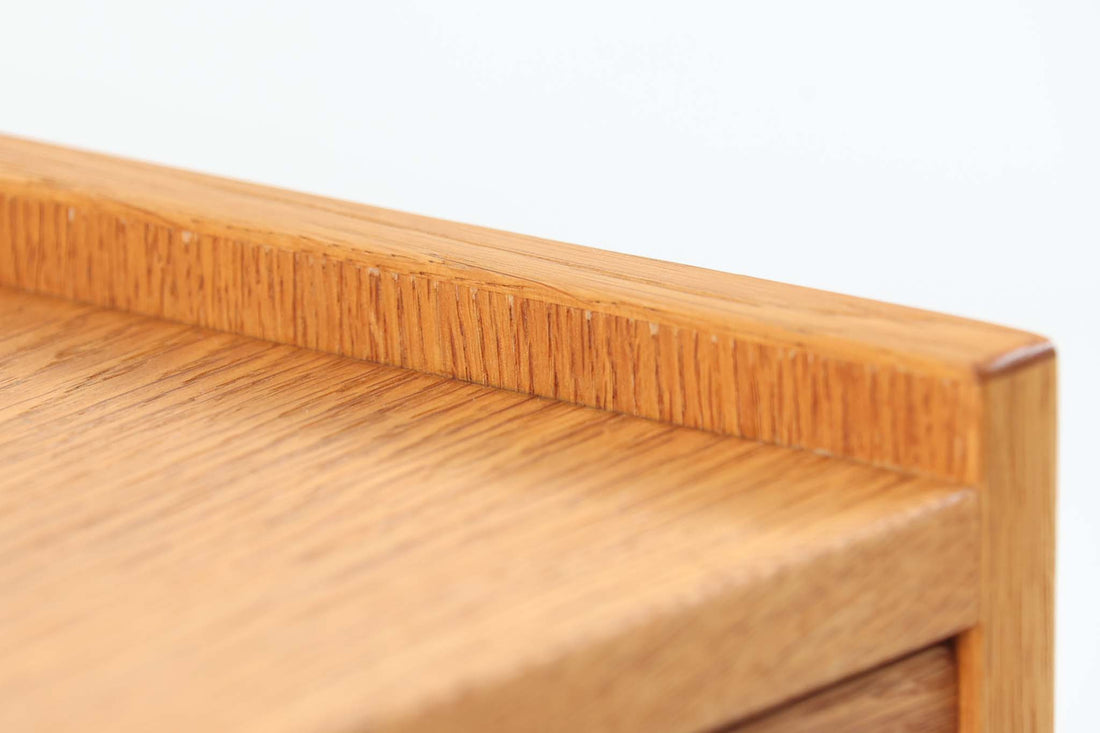 デンマークを代表する家具デザイナー、Hans J. Wegner（ハンス・J・ウェグナー）によってデザインされた、Ry mobler社製のビンテージサイドテーブルです。素材にはあたたかみのあるオーク材が用いられており、北欧らしいシンプルかつ機能的な美しさが感じられます。天板は縁に立ち上がりがあり、物が転がり落ちにくい仕様。引き出しとオープンスペースが組み合わされた実用的な構造で、ベッドサイドやソファ横、玄関周りなど様々なシーンで活躍します。無駄のないデザインと丸脚の柔らかな佇まいが魅力で、ウェグナーデザインならではのバランス感が光る一台です。