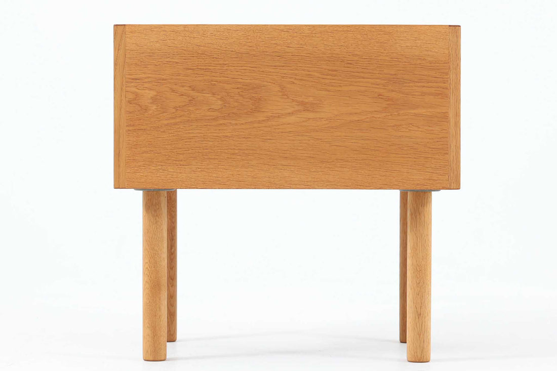 デンマークを代表する家具デザイナー、Hans J. Wegner（ハンス・J・ウェグナー）によってデザインされた、Ry mobler社製のビンテージサイドテーブルです。素材にはあたたかみのあるオーク材が用いられており、北欧らしいシンプルかつ機能的な美しさが感じられます。天板は縁に立ち上がりがあり、物が転がり落ちにくい仕様。引き出しとオープンスペースが組み合わされた実用的な構造で、ベッドサイドやソファ横、玄関周りなど様々なシーンで活躍します。無駄のないデザインと丸脚の柔らかな佇まいが魅力で、ウェグナーデザインならではのバランス感が光る一台です。