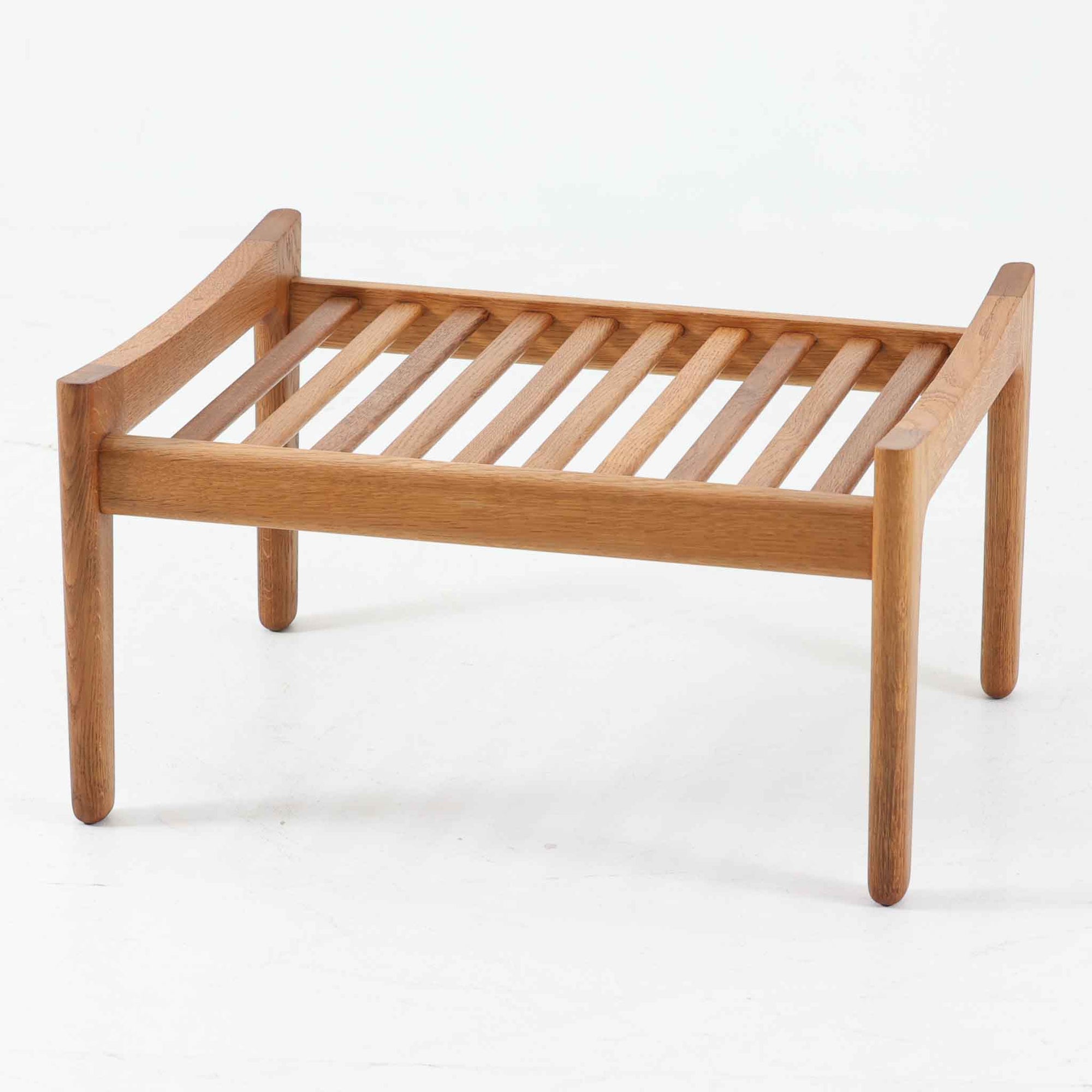 Hans J. WegnerがデザインしGetama社から発表されたGE290オットマンは、堅牢なオーク材のフレームと深みのあるブルーの張地が美しく調和した北欧ビンテージ家具です。直線的でありながら丸みを帯びた脚部が軽快な印象を与え、ソファと組み合わせてフットレストとしてはもちろん、単体でも腰掛けとして使用できます。経年による木肌の風合いと上質な張地が落ち着いた存在感を放つ逸品です。