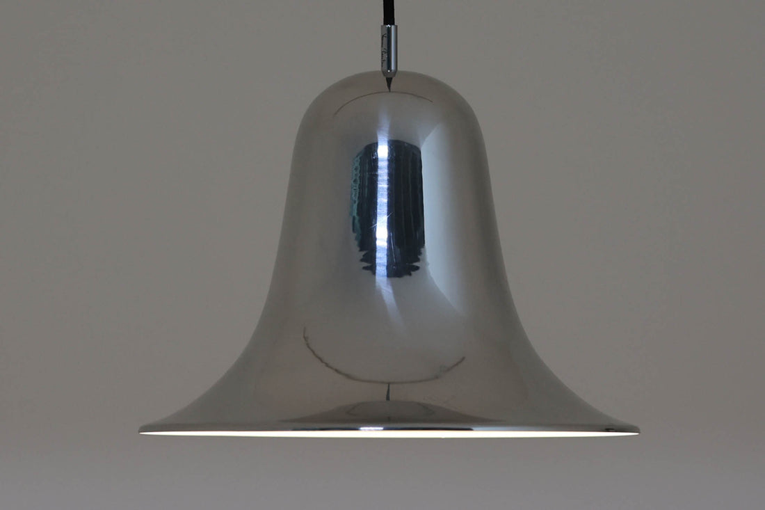 デンマークを代表する照明デザイナーVerner Panton（バーナー・パントン）が手がけた、Frandsen Lighting（フランセン・ライティング）社製のペンダントライトです。なだらかな曲線を描くベル型のシルエットに、ミラーのように周囲を映し出すクローム仕上げが施された、存在感のある一灯。直径約30cmと比較的大ぶりなサイズ感で、1灯でも空間のアクセントとなり、テーブル上や吹き抜け空間などにも映えます。内側はホワイトに塗装されており、点灯時には光を柔らかく広げながらもしっかりとした明るさを確保。Frandsen Lighting社はかつてVerner Pantonとのライセンス契約を結び、このモデルを製造していましたが、現在ではその契約も終了しており、本品のようなオリジナルはヴィンテージ品でしか手に入らなくなっています。特に直径30cmの大きなサイズは現行品では展開されておらず、希少性の高いアイテムとなっています。