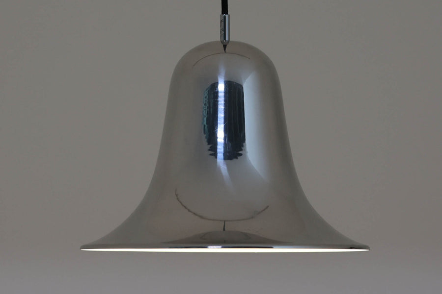デンマークを代表する照明デザイナーVerner Panton（バーナー・パントン）が手がけた、Frandsen Lighting（フランセン・ライティング）社製のペンダントライトです。なだらかな曲線を描くベル型のシルエットに、ミラーのように周囲を映し出すクローム仕上げが施された、存在感のある一灯。直径約30cmと比較的大ぶりなサイズ感で、1灯でも空間のアクセントとなり、テーブル上や吹き抜け空間などにも映えます。内側はホワイトに塗装されており、点灯時には光を柔らかく広げながらもしっかりとした明るさを確保。Frandsen Lighting社はかつてVerner Pantonとのライセンス契約を結び、このモデルを製造していましたが、現在ではその契約も終了しており、本品のようなオリジナルはヴィンテージ品でしか手に入らなくなっています。特に直径30cmの大きなサイズは現行品では展開されておらず、希少性の高いアイテムとなっています。