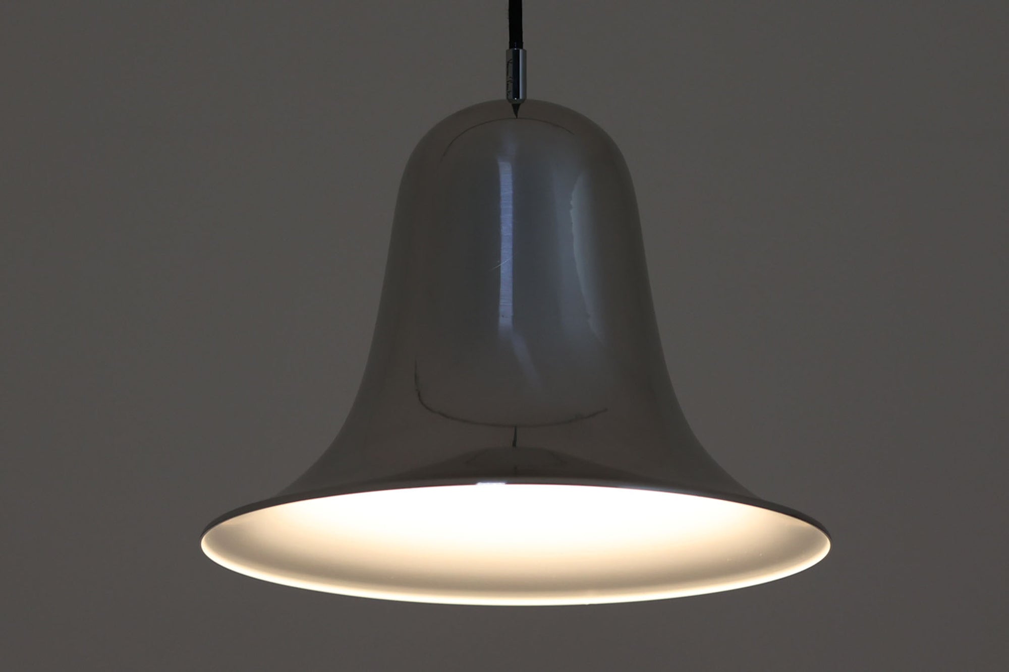 デンマークを代表する照明デザイナーVerner Panton（バーナー・パントン）が手がけた、Frandsen Lighting（フランセン・ライティング）社製のペンダントライトです。なだらかな曲線を描くベル型のシルエットに、ミラーのように周囲を映し出すクローム仕上げが施された、存在感のある一灯。直径約30cmと比較的大ぶりなサイズ感で、1灯でも空間のアクセントとなり、テーブル上や吹き抜け空間などにも映えます。内側はホワイトに塗装されており、点灯時には光を柔らかく広げながらもしっかりとした明るさを確保。Frandsen Lighting社はかつてVerner Pantonとのライセンス契約を結び、このモデルを製造していましたが、現在ではその契約も終了しており、本品のようなオリジナルはヴィンテージ品でしか手に入らなくなっています。特に直径30cmの大きなサイズは現行品では展開されておらず、希少性の高いアイテムとなっています。