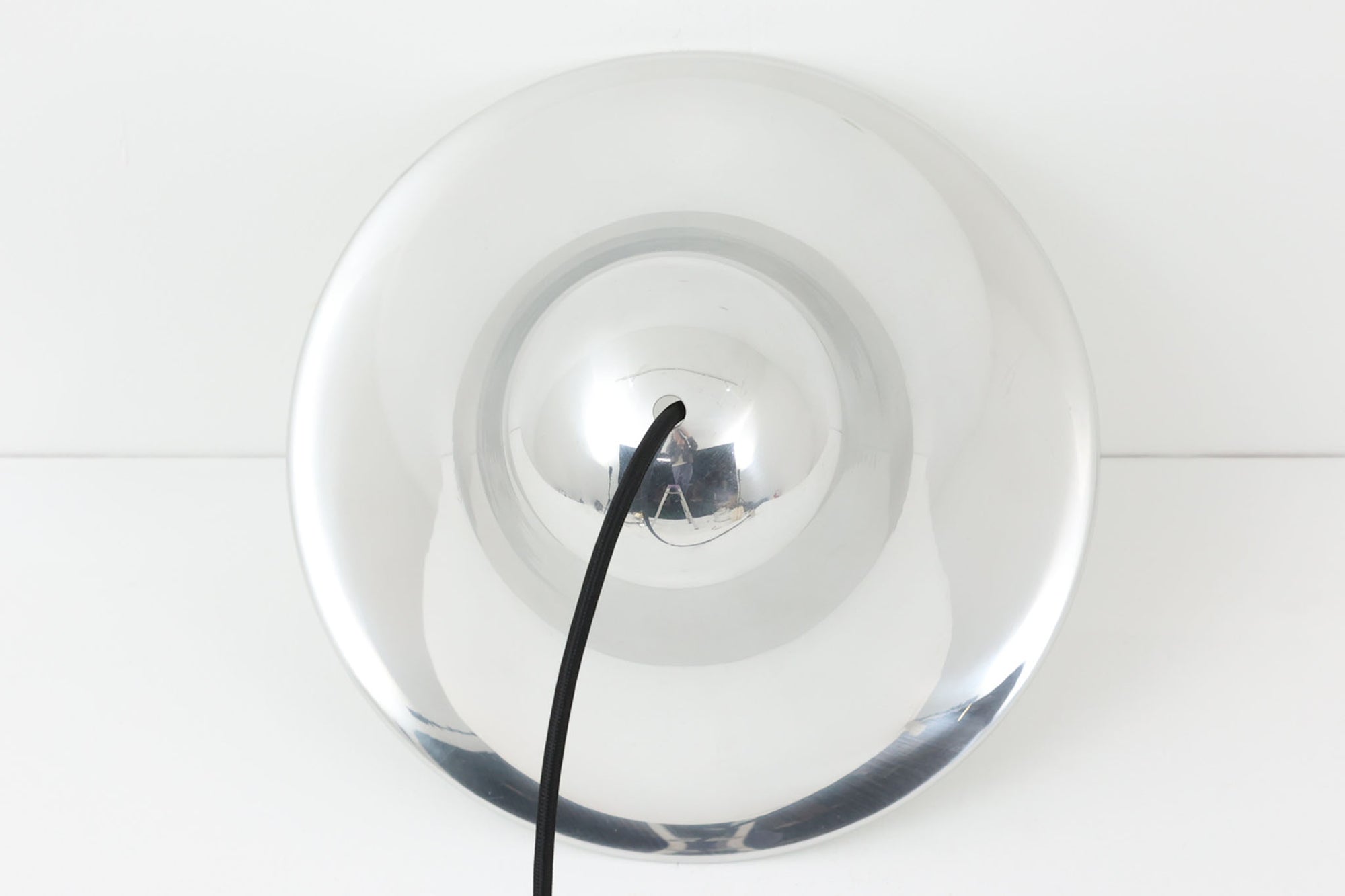 デンマークを代表する照明デザイナーVerner Panton（バーナー・パントン）が手がけた、Frandsen Lighting（フランセン・ライティング）社製のペンダントライトです。なだらかな曲線を描くベル型のシルエットに、ミラーのように周囲を映し出すクローム仕上げが施された、存在感のある一灯。直径約30cmと比較的大ぶりなサイズ感で、1灯でも空間のアクセントとなり、テーブル上や吹き抜け空間などにも映えます。内側はホワイトに塗装されており、点灯時には光を柔らかく広げながらもしっかりとした明るさを確保。Frandsen Lighting社はかつてVerner Pantonとのライセンス契約を結び、このモデルを製造していましたが、現在ではその契約も終了しており、本品のようなオリジナルはヴィンテージ品でしか手に入らなくなっています。特に直径30cmの大きなサイズは現行品では展開されておらず、希少性の高いアイテムとなっています。