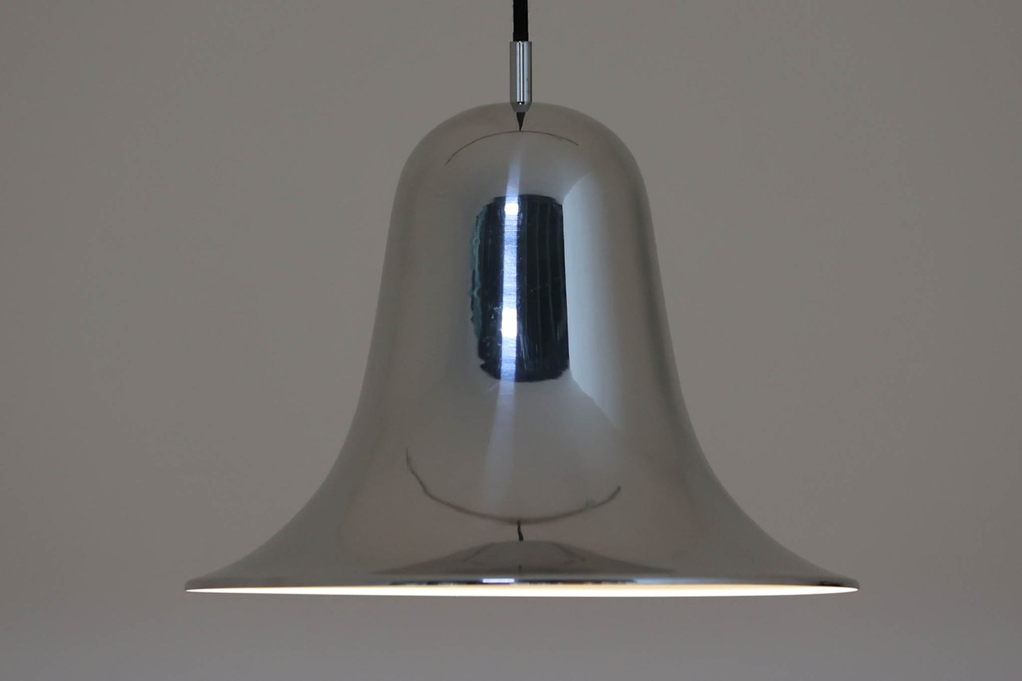 デンマークを代表する照明デザイナーVerner Panton（バーナー・パントン）が手がけた、Frandsen Lighting（フランセン・ライティング）社製のペンダントライトです。なだらかな曲線を描くベル型のシルエットに、ミラーのように周囲を映し出すクローム仕上げが施された、存在感のある一灯。直径約30cmと比較的大ぶりなサイズ感で、1灯でも空間のアクセントとなり、テーブル上や吹き抜け空間などにも映えます。内側はホワイトに塗装されており、点灯時には光を柔らかく広げながらもしっかりとした明るさを確保。Frandsen Lighting社はかつてVerner Pantonとのライセンス契約を結び、このモデルを製造していましたが、現在ではその契約も終了しており、本品のようなオリジナルはヴィンテージ品でしか手に入らなくなっています。特に直径30cmの大きなサイズは現行品では展開されておらず、希少性の高いアイテムとなっています。