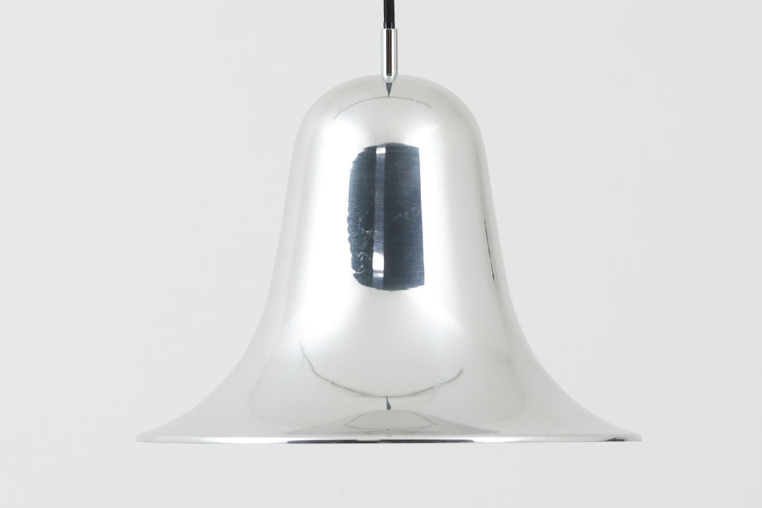 デンマークを代表する照明デザイナーVerner Panton（バーナー・パントン）が手がけた、Frandsen Lighting（フランセン・ライティング）社製のペンダントライトです。なだらかな曲線を描くベル型のシルエットに、ミラーのように周囲を映し出すクローム仕上げが施された、存在感のある一灯。直径約30cmと比較的大ぶりなサイズ感で、1灯でも空間のアクセントとなり、テーブル上や吹き抜け空間などにも映えます。内側はホワイトに塗装されており、点灯時には光を柔らかく広げながらもしっかりとした明るさを確保。Frandsen Lighting社はかつてVerner Pantonとのライセンス契約を結び、このモデルを製造していましたが、現在ではその契約も終了しており、本品のようなオリジナルはヴィンテージ品でしか手に入らなくなっています。特に直径30cmの大きなサイズは現行品では展開されておらず、希少性の高いアイテムとなっています。