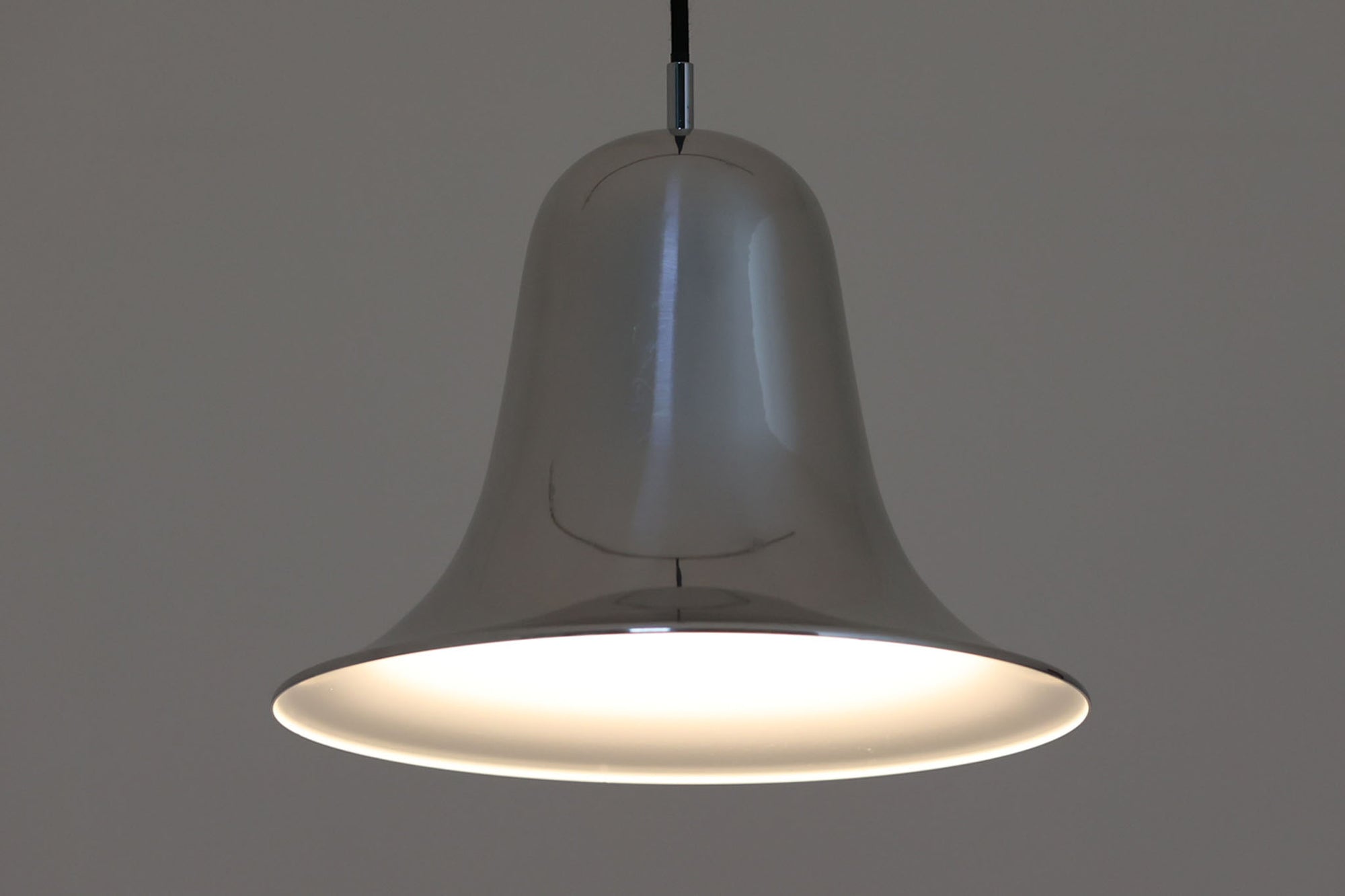 デンマークを代表する照明デザイナーVerner Panton（バーナー・パントン）が手がけた、Frandsen Lighting（フランセン・ライティング）社製のペンダントライトです。なだらかな曲線を描くベル型のシルエットに、ミラーのように周囲を映し出すクローム仕上げが施された、存在感のある一灯。直径約30cmと比較的大ぶりなサイズ感で、1灯でも空間のアクセントとなり、テーブル上や吹き抜け空間などにも映えます。内側はホワイトに塗装されており、点灯時には光を柔らかく広げながらもしっかりとした明るさを確保。Frandsen Lighting社はかつてVerner Pantonとのライセンス契約を結び、このモデルを製造していましたが、現在ではその契約も終了しており、本品のようなオリジナルはヴィンテージ品でしか手に入らなくなっています。特に直径30cmの大きなサイズは現行品では展開されておらず、希少性の高いアイテムとなっています。