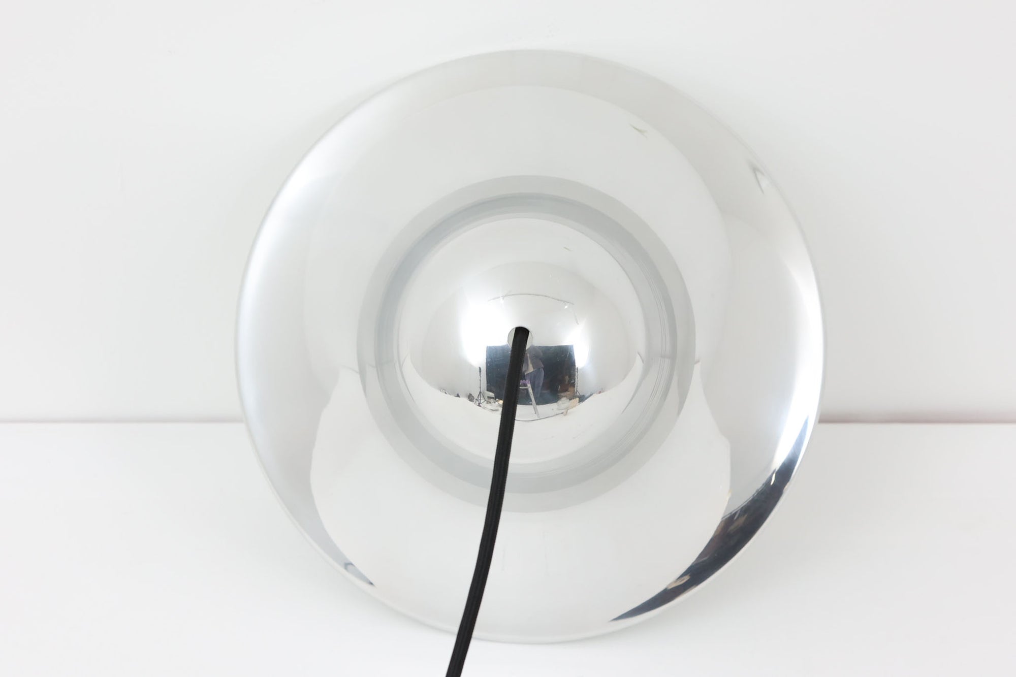 デンマークを代表する照明デザイナーVerner Panton（バーナー・パントン）が手がけた、Frandsen Lighting（フランセン・ライティング）社製のペンダントライトです。なだらかな曲線を描くベル型のシルエットに、ミラーのように周囲を映し出すクローム仕上げが施された、存在感のある一灯。直径約30cmと比較的大ぶりなサイズ感で、1灯でも空間のアクセントとなり、テーブル上や吹き抜け空間などにも映えます。内側はホワイトに塗装されており、点灯時には光を柔らかく広げながらもしっかりとした明るさを確保。Frandsen Lighting社はかつてVerner Pantonとのライセンス契約を結び、このモデルを製造していましたが、現在ではその契約も終了しており、本品のようなオリジナルはヴィンテージ品でしか手に入らなくなっています。特に直径30cmの大きなサイズは現行品では展開されておらず、希少性の高いアイテムとなっています。