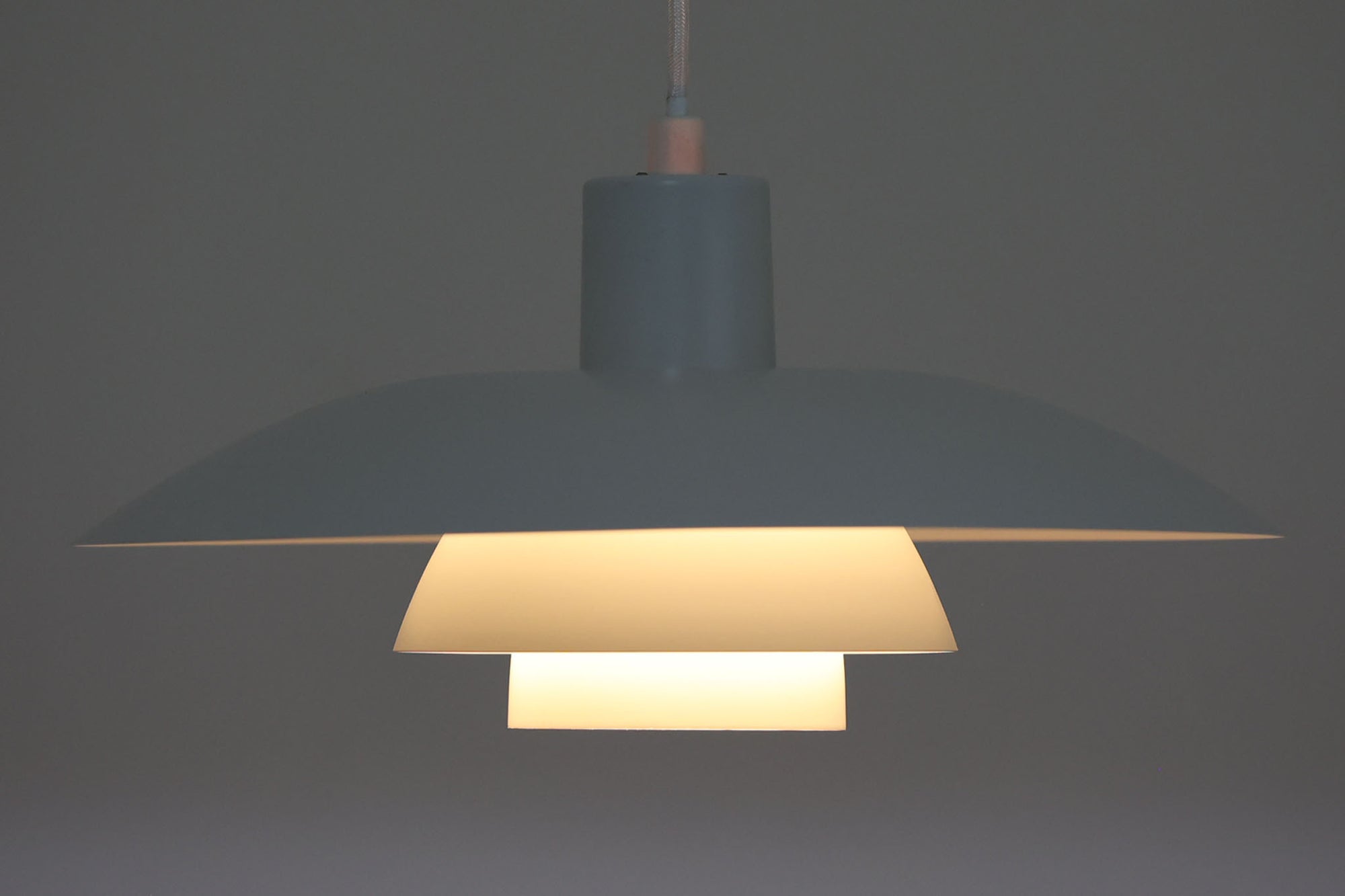 北欧照明の巨匠Poul Henningsenによってデザインされた「PH4」ペンダントライト。Louis Poulsen社製で、光を効率よく拡散させる3枚シェード構造が特徴。内側にオレンジのリフレクターを備えており、暖かく落ち着いた光を演出します。シェード表面には経年に伴う擦れや細かい傷、塗装の薄れが見られますが、ビンテージらしい味わいを感じられる一品です。リビングやダイニング、カウンター上などにおすすめのサイズ感です。