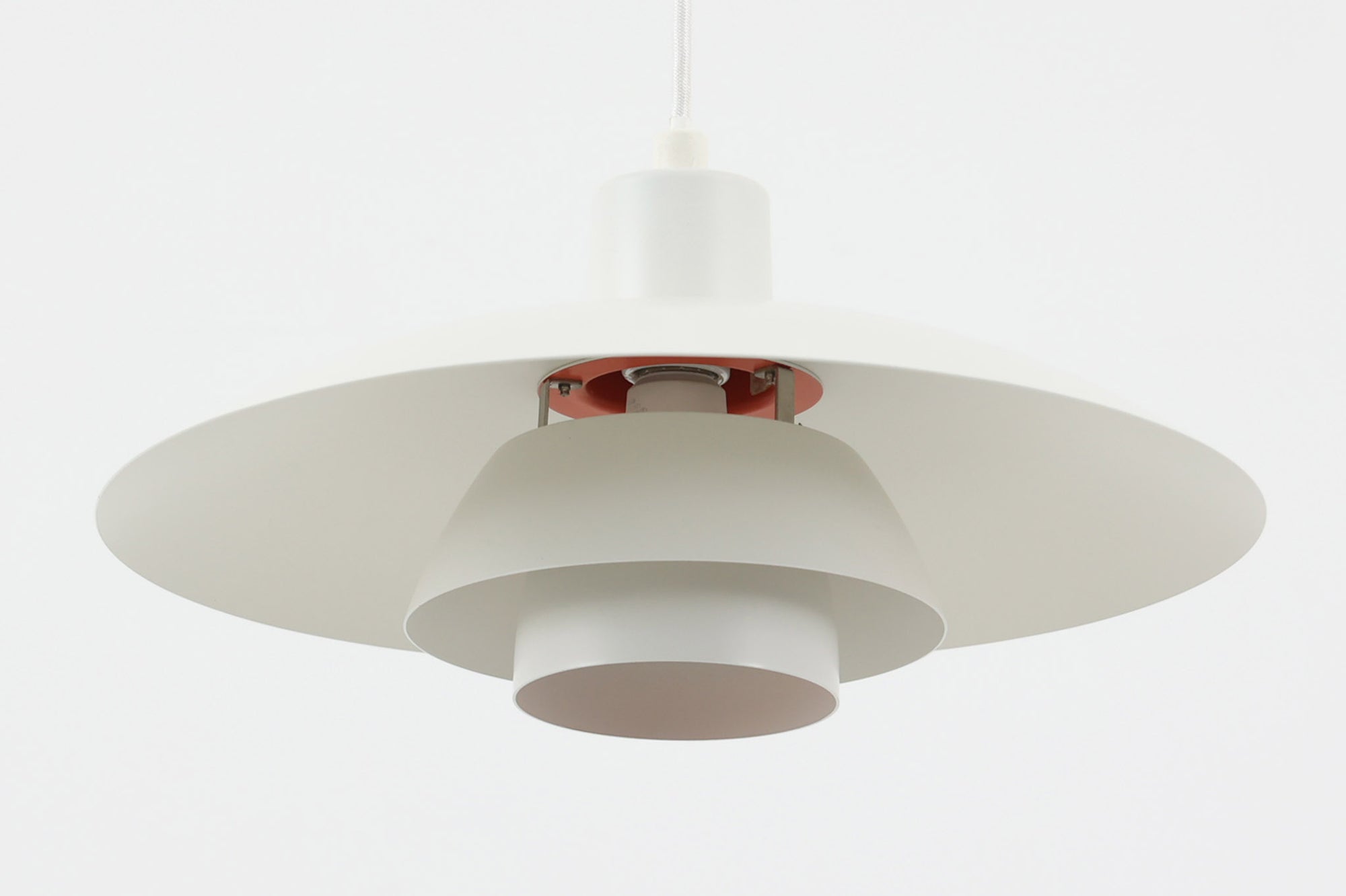 北欧照明の巨匠Poul Henningsenによってデザインされた「PH4」ペンダントライト。Louis Poulsen社製で、光を効率よく拡散させる3枚シェード構造が特徴。内側にオレンジのリフレクターを備えており、暖かく落ち着いた光を演出します。シェード表面には経年に伴う擦れや細かい傷、塗装の薄れが見られますが、ビンテージらしい味わいを感じられる一品です。リビングやダイニング、カウンター上などにおすすめのサイズ感です。