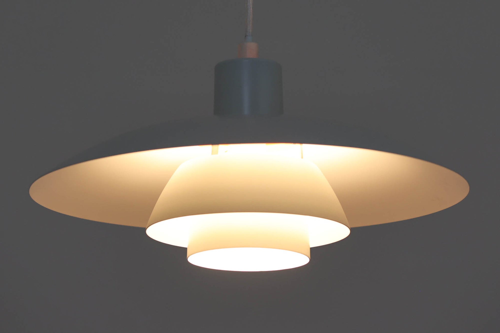 北欧照明の巨匠Poul Henningsenによってデザインされた「PH4」ペンダントライト。Louis Poulsen社製で、光を効率よく拡散させる3枚シェード構造が特徴。内側にオレンジのリフレクターを備えており、暖かく落ち着いた光を演出します。シェード表面には経年に伴う擦れや細かい傷、塗装の薄れが見られますが、ビンテージらしい味わいを感じられる一品です。リビングやダイニング、カウンター上などにおすすめのサイズ感です。