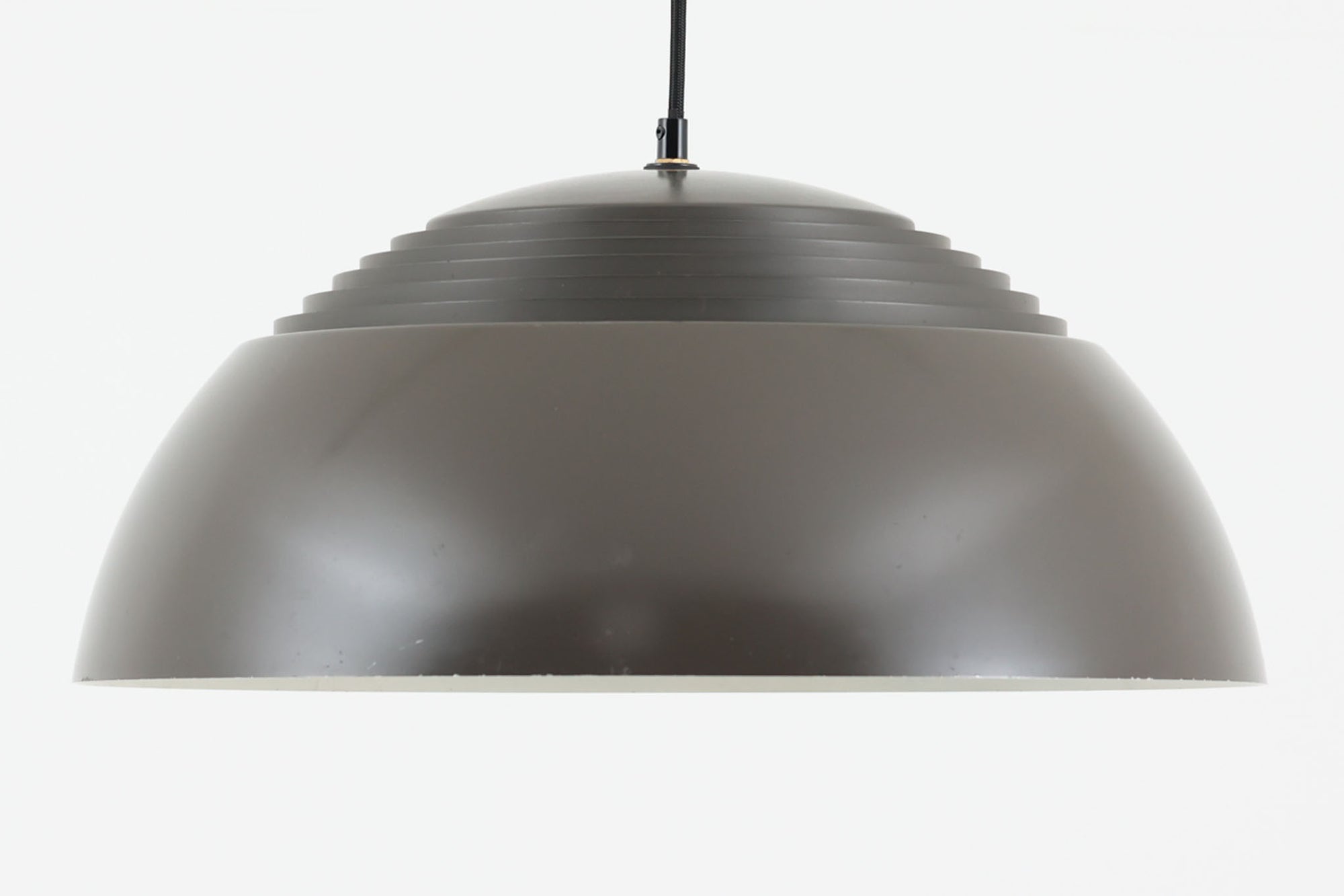アルネ・ヤコブセンによってデザインされ、Louis Poulsen（ルイスポールセン）より製造されたAJロイヤル ペンダントライト。こちらは希少なグラファイトグレーカラーで、落ち着いたトーンが空間にシックな雰囲気を演出します。直径50cmの大型サイズで、光源を遮る構造と放射状に配置されたルーバーにより、眩しさを抑えた柔らかい光が空間全体を包み込みます。点灯時には上部のスリットから漏れる光も美しく、デザイン性と機能性を兼ね備えた一品です。外観には小傷や使用感がありますが、ビンテージならではの風合いとしてお楽しみいただけます。
