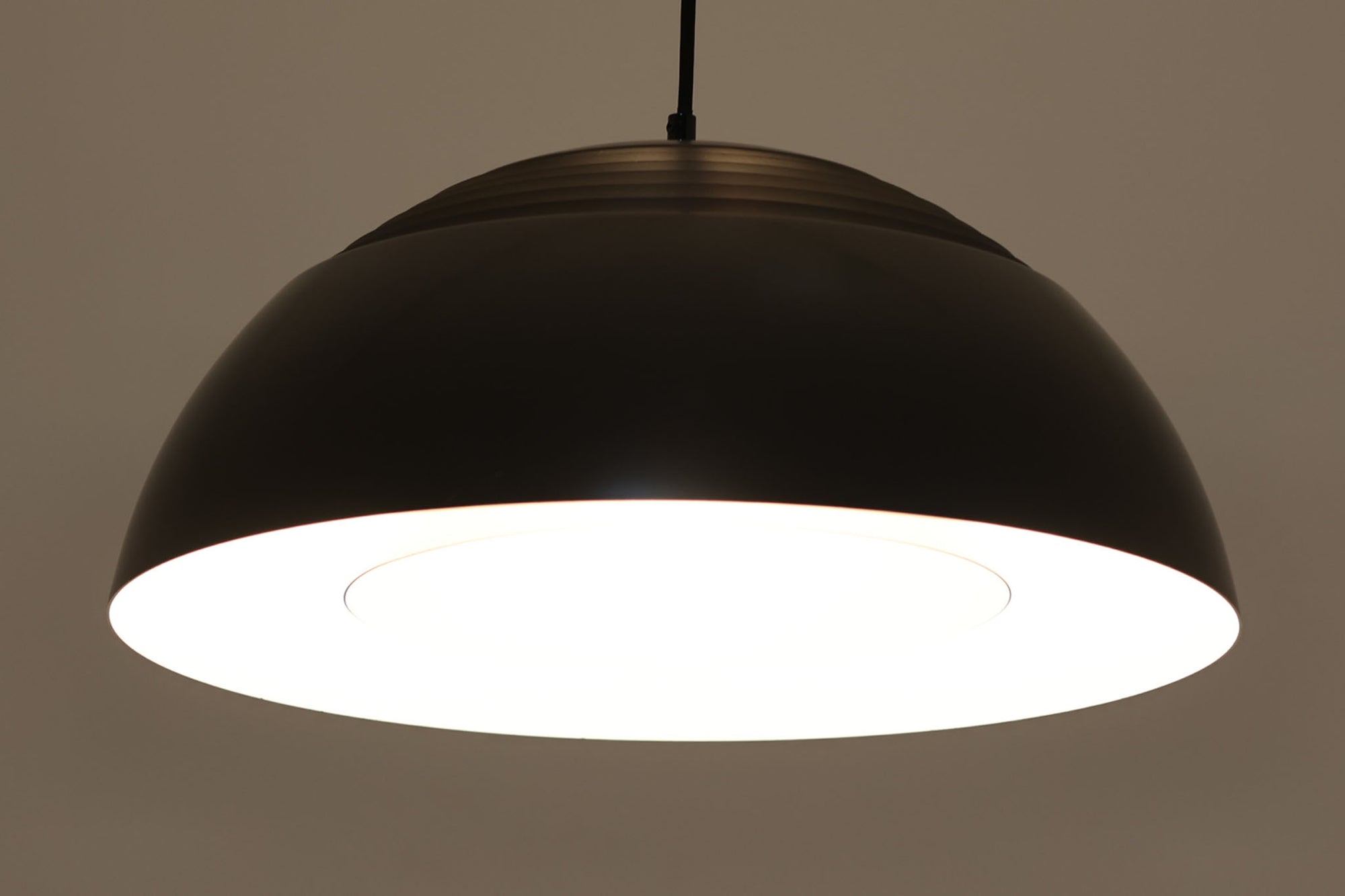 アルネ・ヤコブセンによってデザインされ、Louis Poulsen（ルイスポールセン）より製造されたAJロイヤル ペンダントライト。こちらは希少なグラファイトグレーカラーで、落ち着いたトーンが空間にシックな雰囲気を演出します。直径50cmの大型サイズで、光源を遮る構造と放射状に配置されたルーバーにより、眩しさを抑えた柔らかい光が空間全体を包み込みます。点灯時には上部のスリットから漏れる光も美しく、デザイン性と機能性を兼ね備えた一品です。外観には小傷や使用感がありますが、ビンテージならではの風合いとしてお楽しみいただけます。